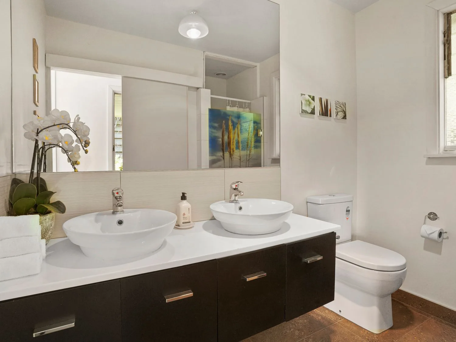 Un baño con dos lavabos, un inodoro, un espejo grande y una ventana en Kaioruru View - Diamond Harbour Holiday Home, en Diamond Harbour