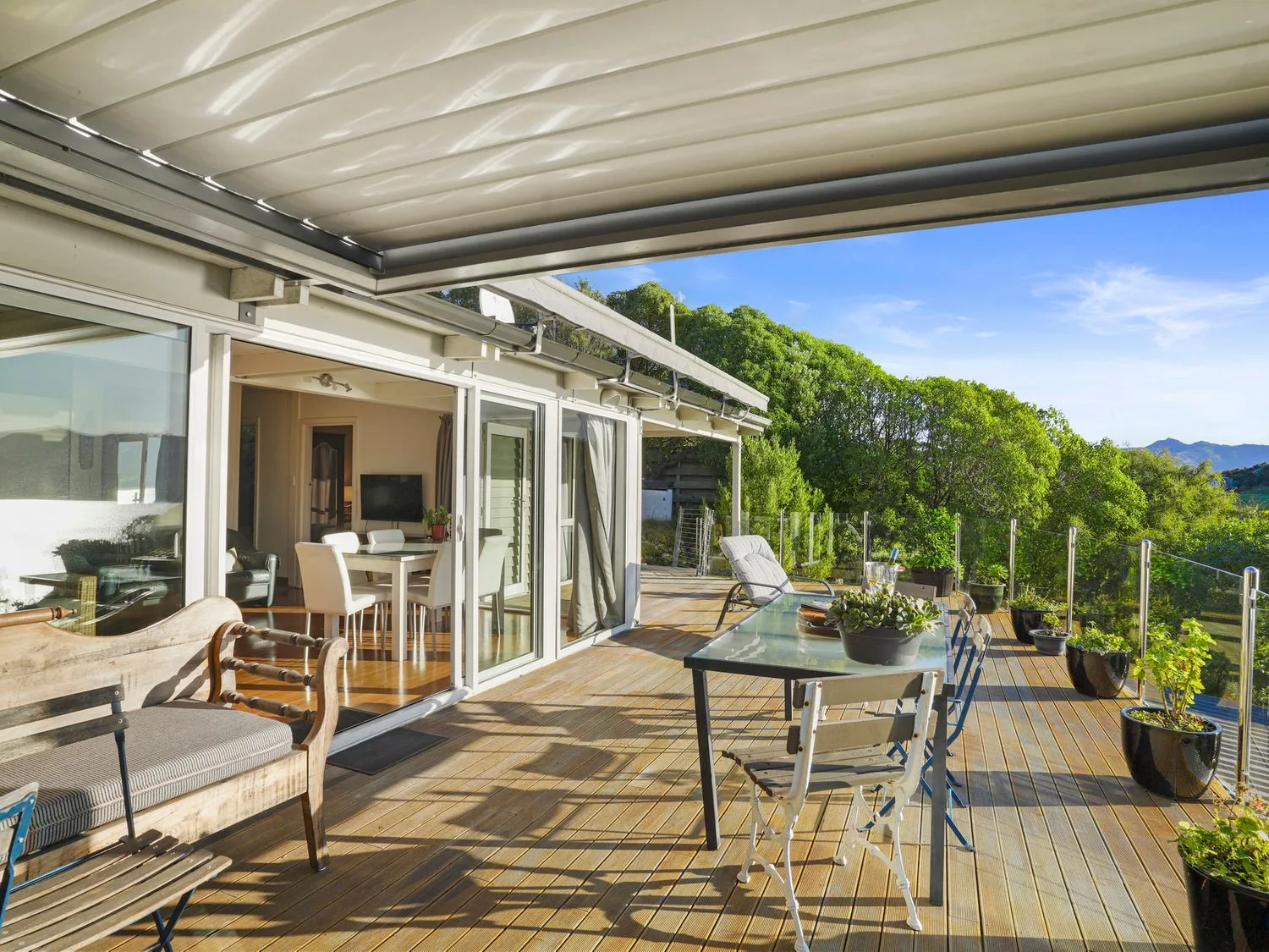 Una terraza de madera con sillas de exterior, una mesa con plantas y una tumbona, con vistas a la vegetación en Kaioruru View - Diamond Harbour Holiday Home, en Diamond Harbour