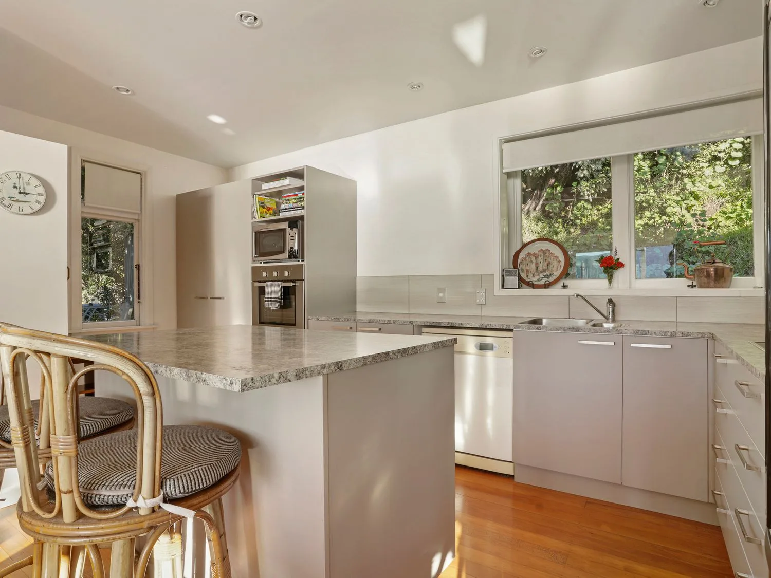 Una cocina luminosa con isla de piedra, horno empotrado y una ventana sobre el fregadero.