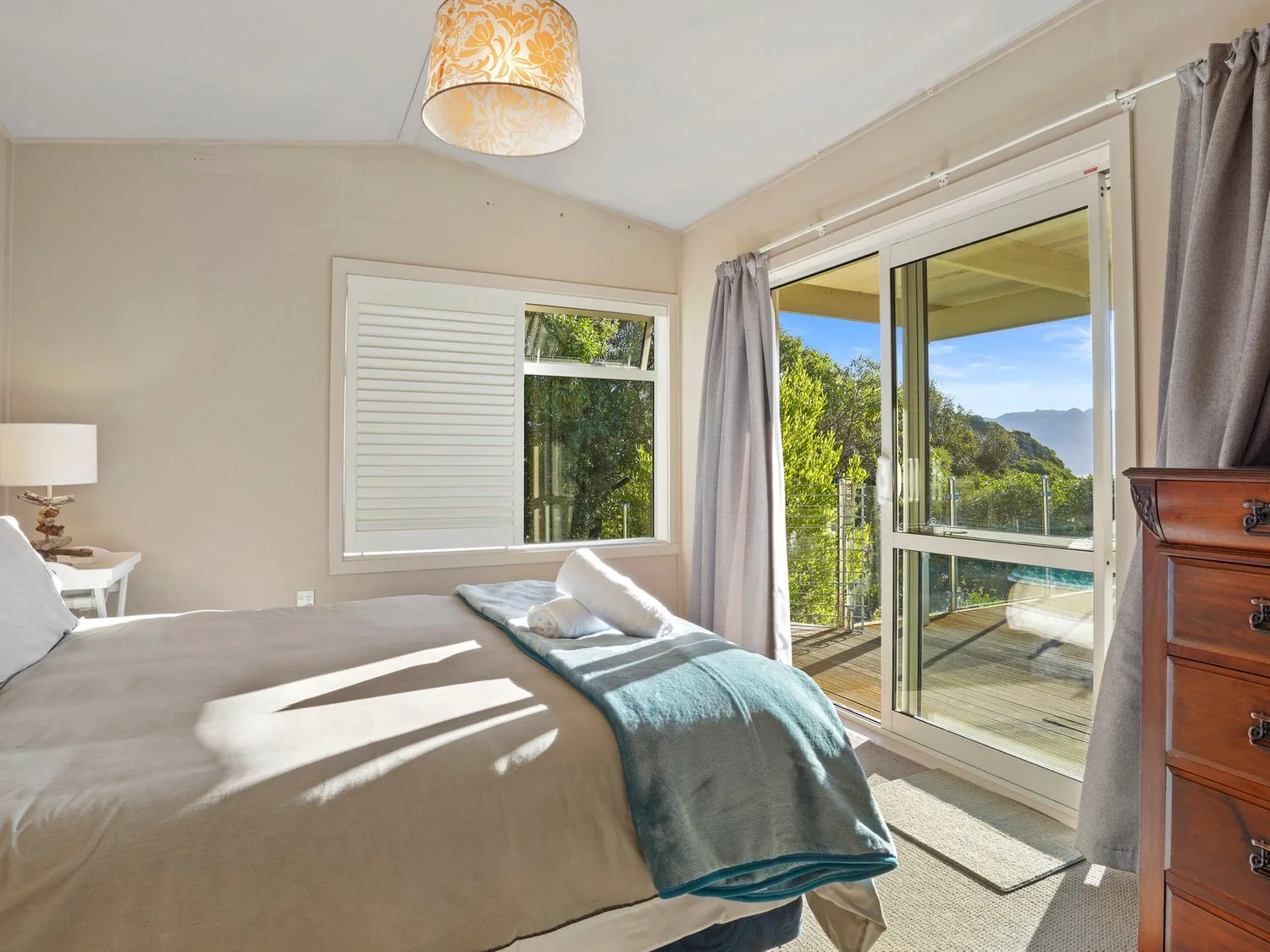 Un dormitorio con una cama junto a una ventana con contraventanas y puertas correderas de cristal abiertas.