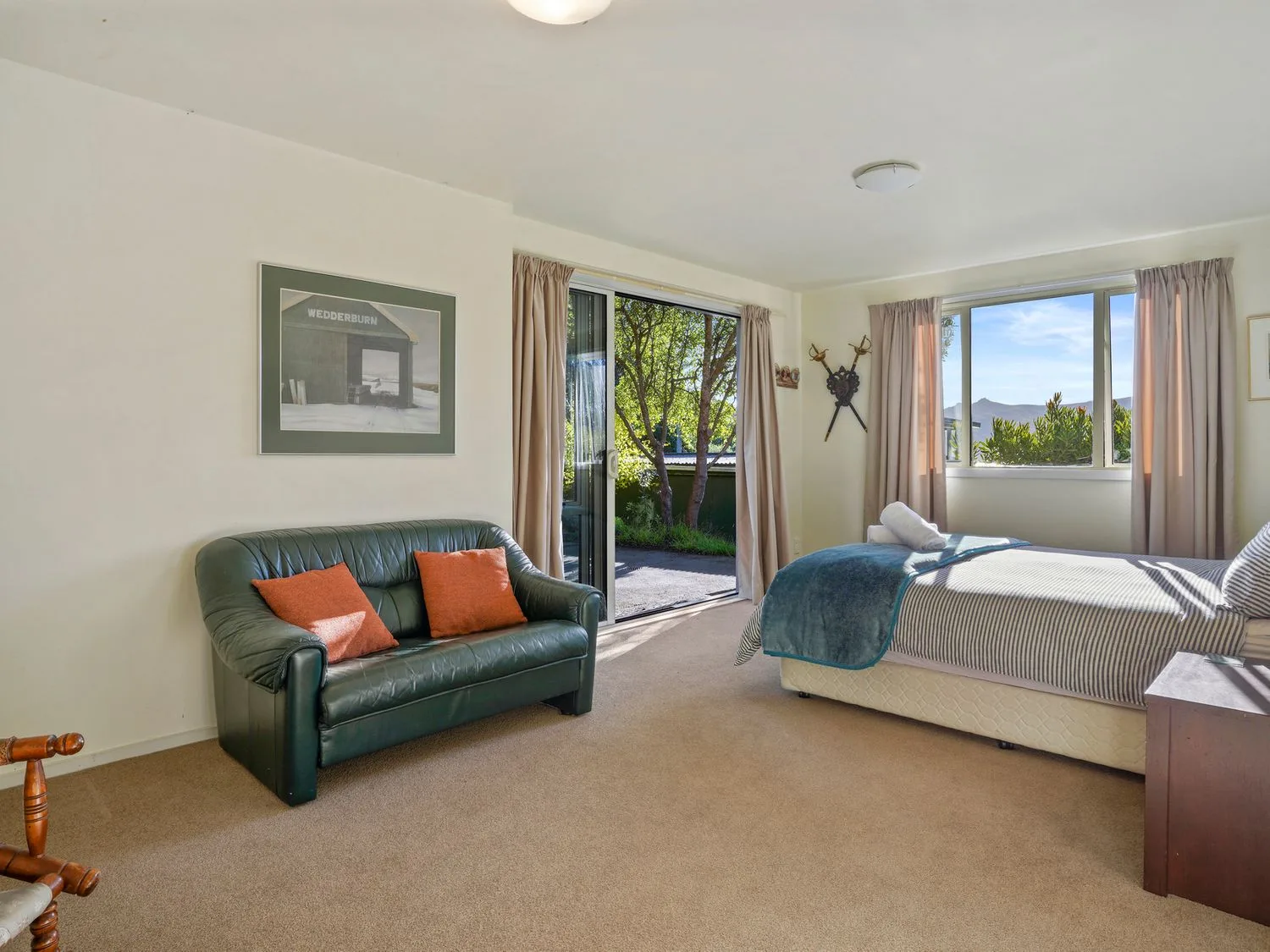 Un dormitorio con una cama, un sofá de cuero verde con cojines naranjas, una ventana con cortinas y una puerta corredera de cristal en Kaioruru View Diamond Harbour Holiday Home