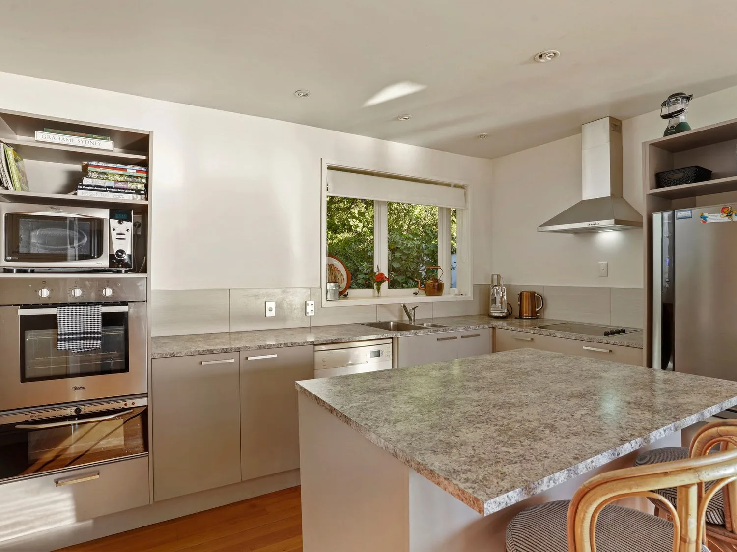 Una cocina con una isla con encimera de mármol, dos sillas de madera, una ventana, un microondas, un lavavajillas y un refrigerador en Kaioruru View - Diamond Harbour Holiday Home, en Diamond Harbour