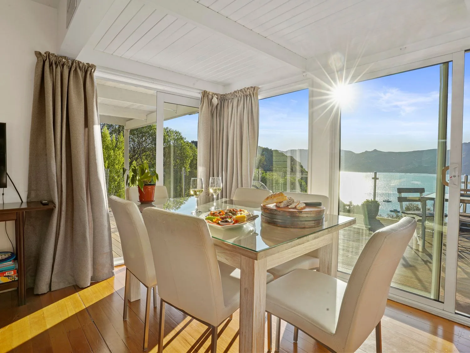 A dining area with a glass table and chairs beside large windows overlooking the water.