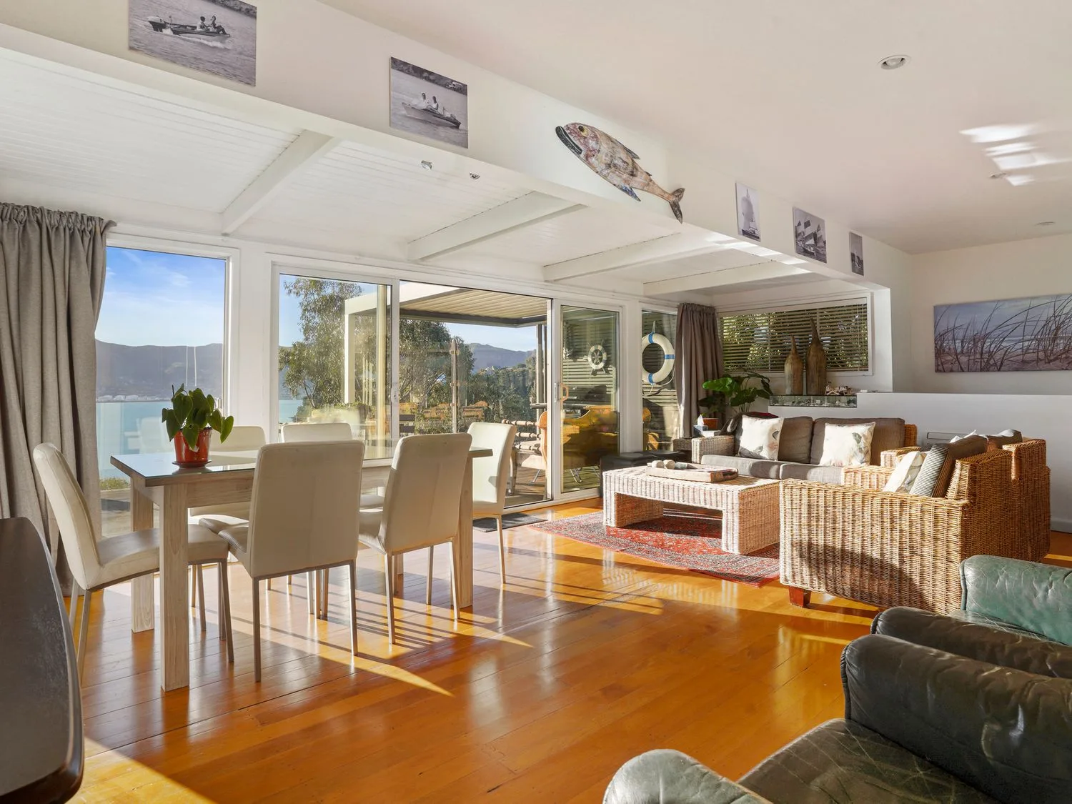 A living and dining area with a wooden dining table with six chairs a wicker sofa set a coffee table and sliding glass doors at Kaioruru View Diamond Harbour