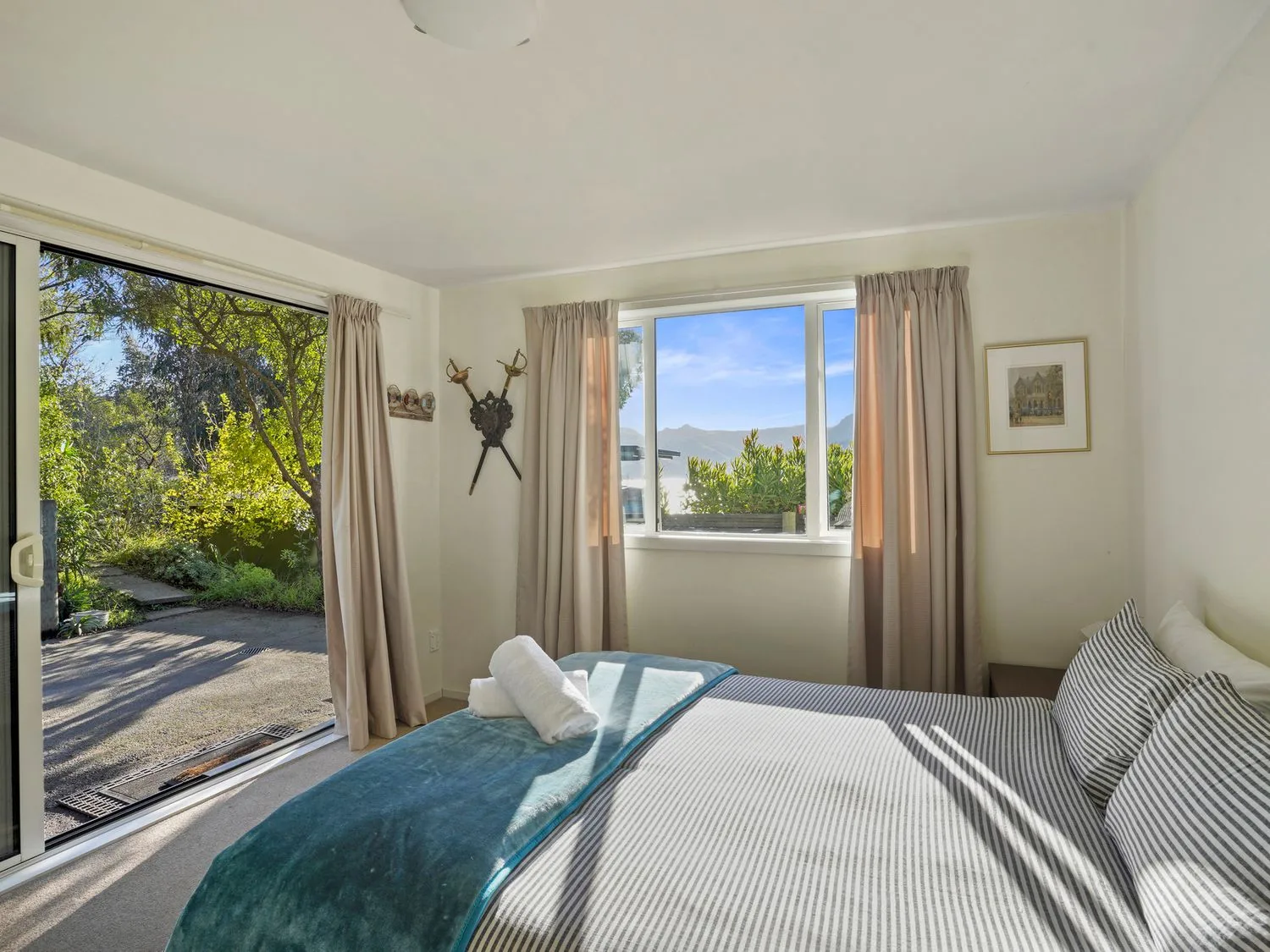 Un dormitorio con una cama, ropa de cama a rayas, una puerta corredera de cristal y una ventana con cortinas beige en Kaioruru View Diamond Harbour