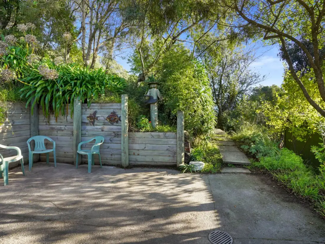 Un patio exterior con sillas verdes junto a un muro de madera y un sendero de jardín.