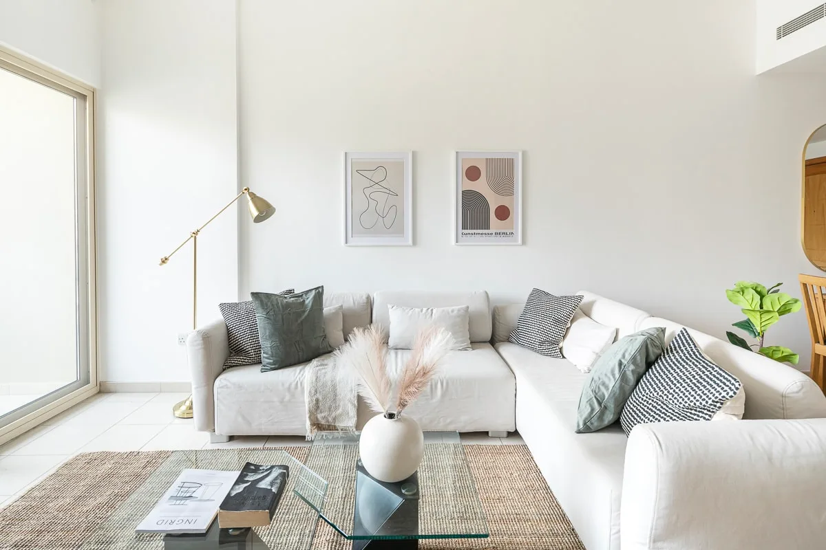 A bright living room with a white sectional sofa and glass coffee table.