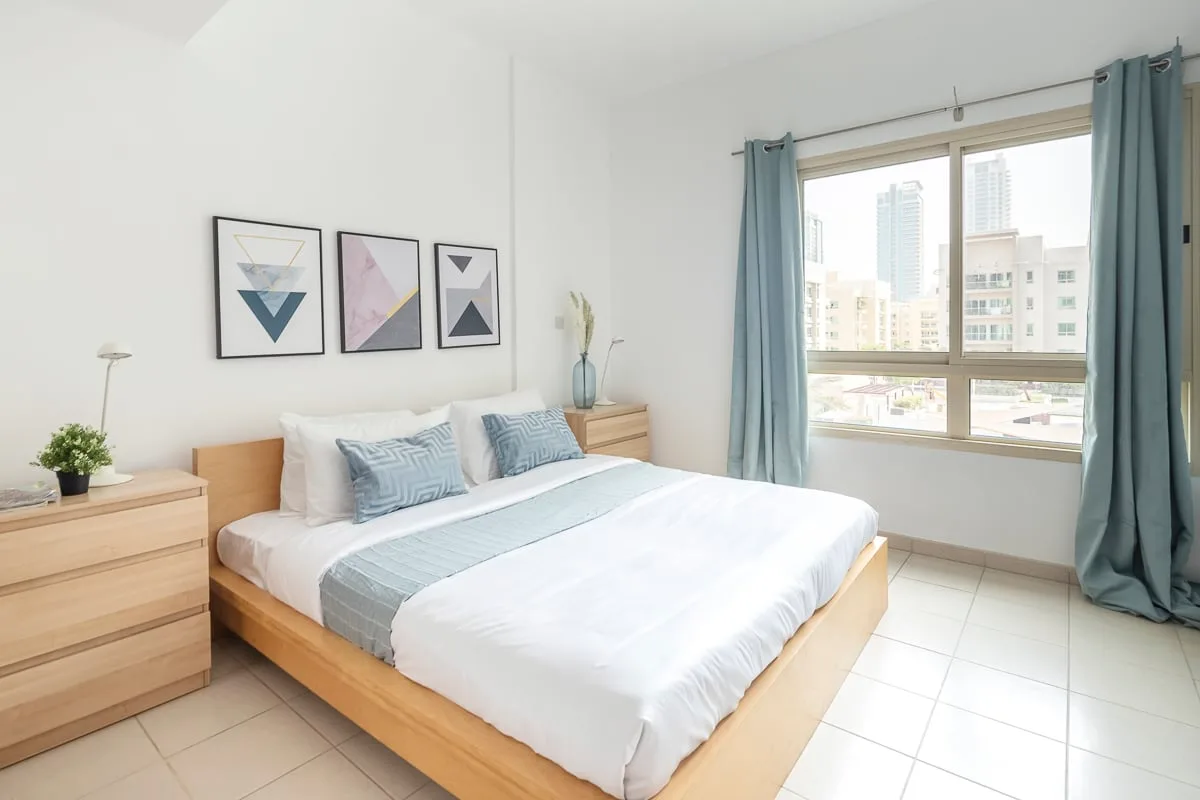 A bright bedroom with a neatly made bed and large window.