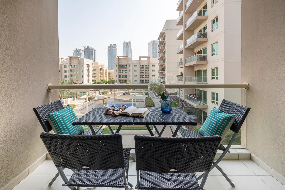 Una zona de estar en un balcón con una mesa frente a edificios de apartamentos.