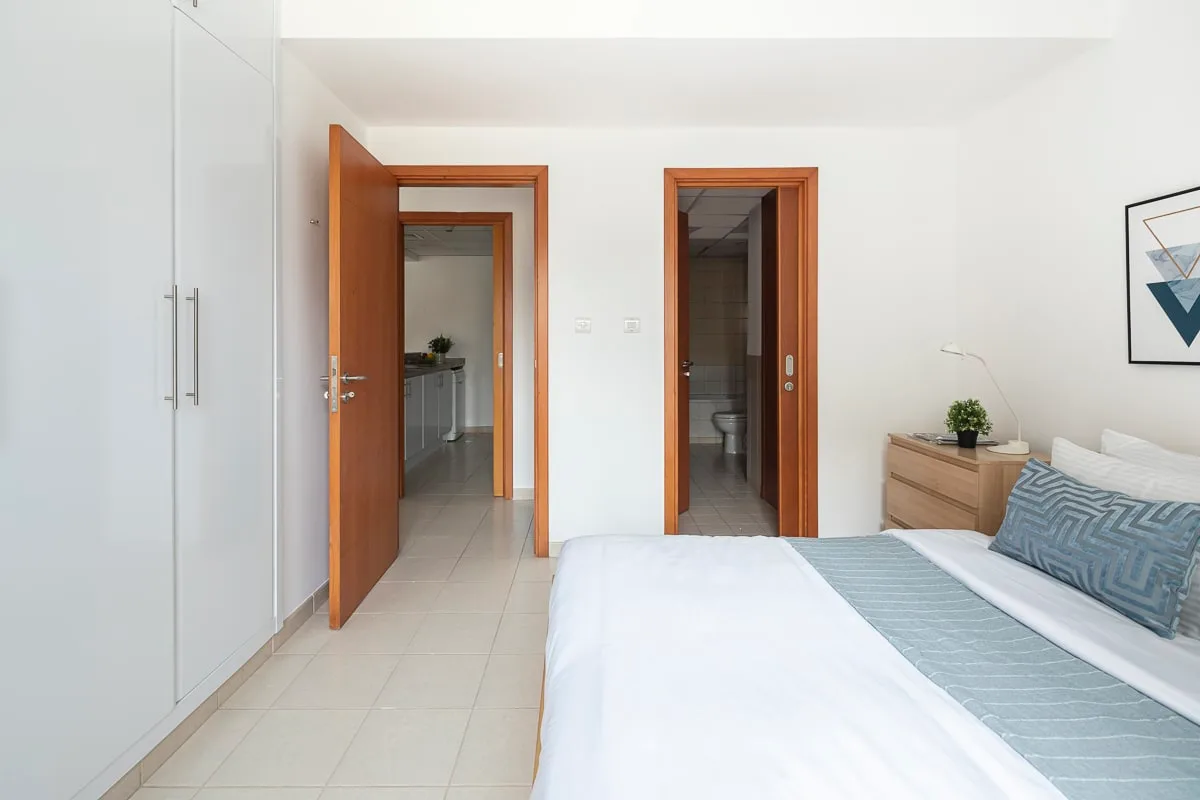 A bright bedroom with a neatly made bed and two open doorways.