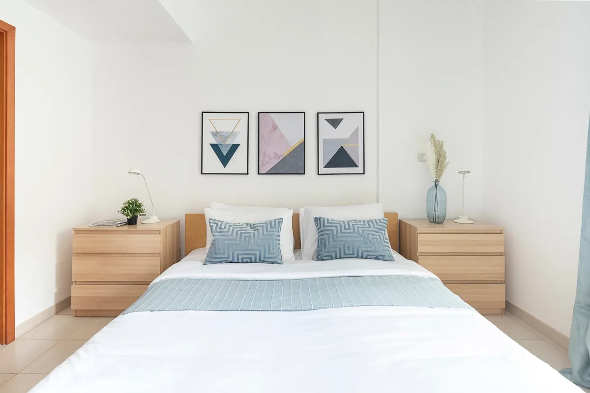 A bedroom with a neatly made bed, bedside tables, and framed geometric art.