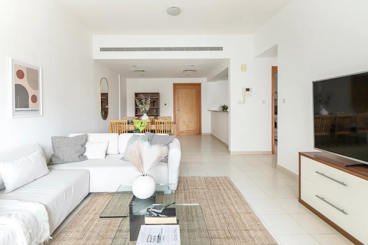A bright living room with a white sectional, a rug, and a dining area beyond.