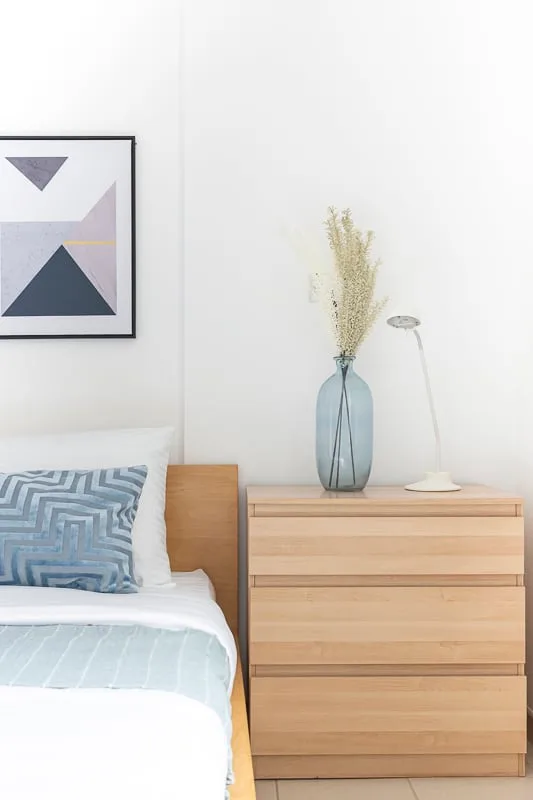 A bedroom with a light wood dresser, bedside lamp, and framed geometric artwork.
