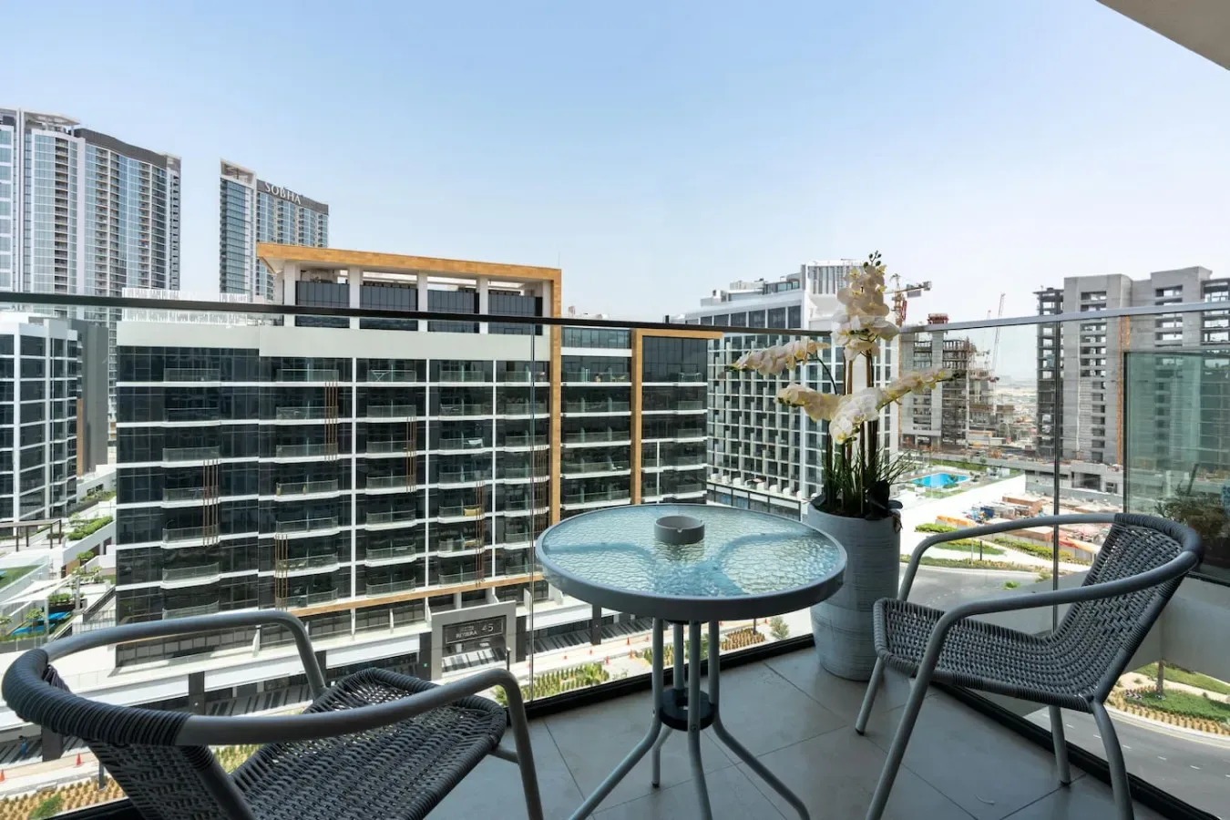 A balcony seating area overlooks modern buildings, with a small round table and potted plant.