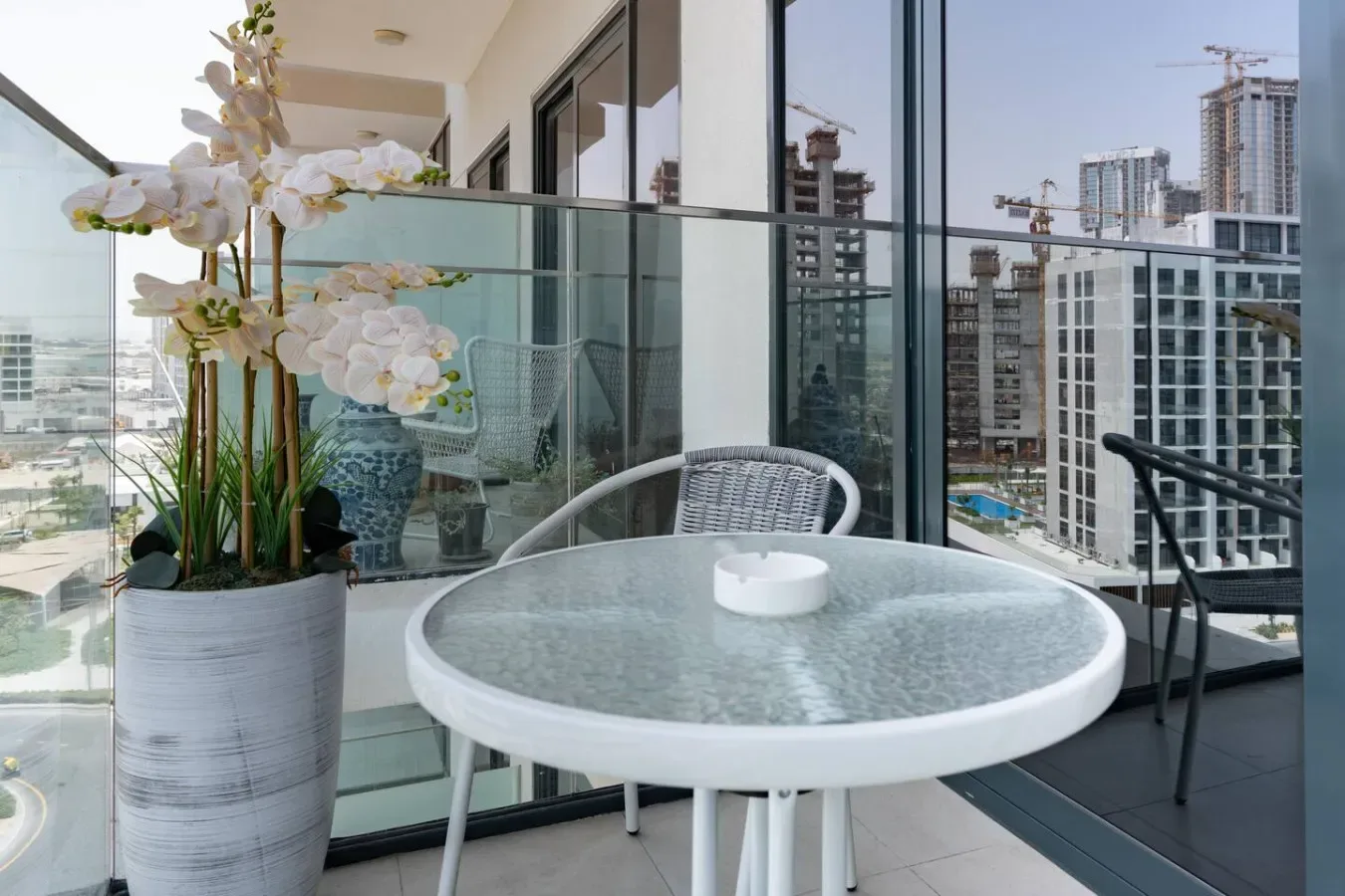 Una zona de estar en un balcón con una mesa redonda y orquídeas en maceta, frente a edificios cercanos.