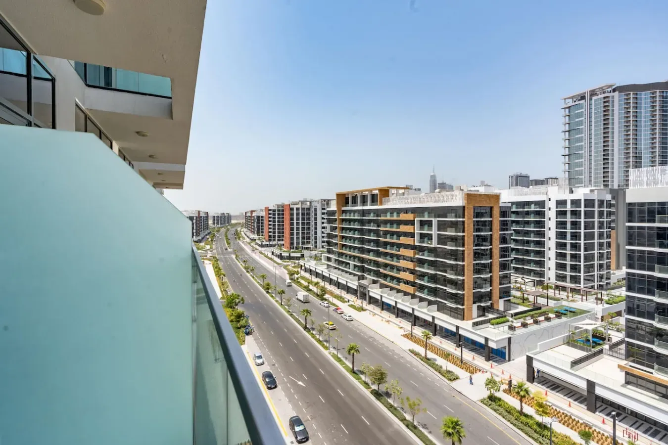 Un balcón da a una amplia avenida urbana bordeada de edificios de apartamentos modernos.