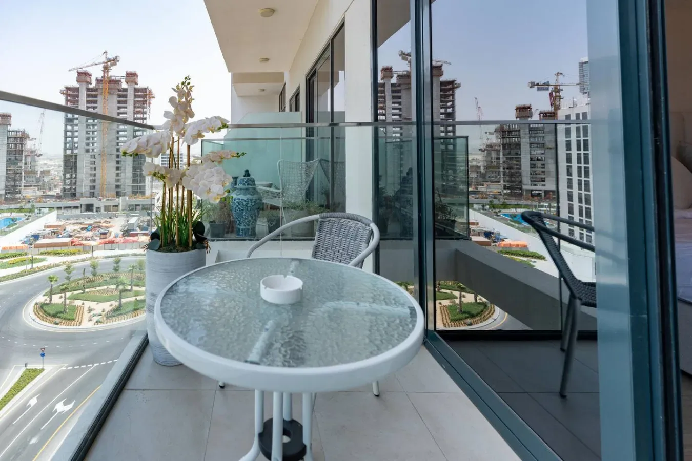 Una zona de estar en el balcón con una mesa redonda de vidrio y plantas en macetas.