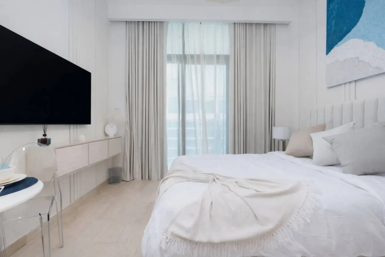 Un dormitorio luminoso con una cama grande, una ventana alta y un televisor.