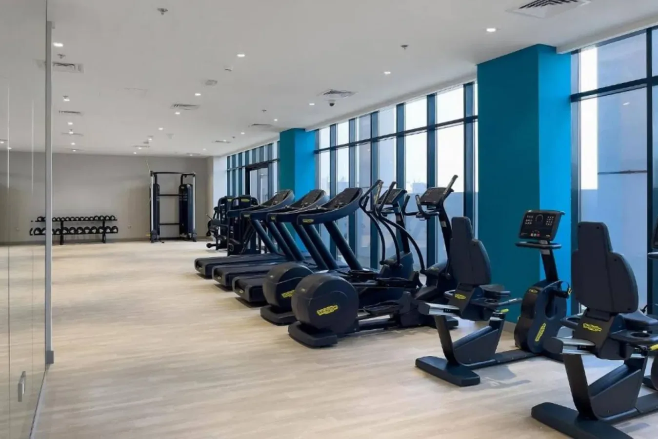 Un gimnasio con máquinas de ejercicio cardiovascular junto a grandes ventanales.