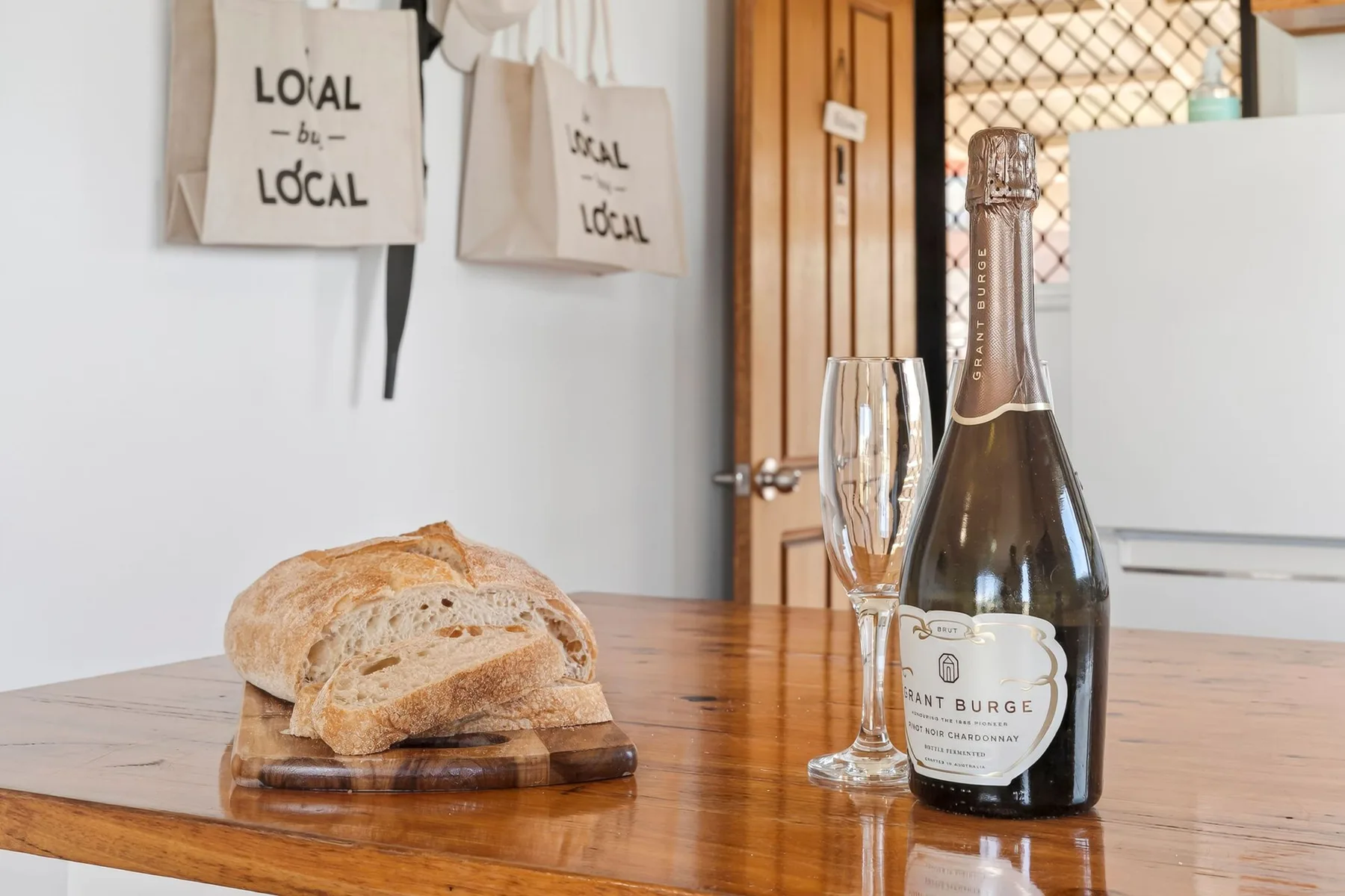 A dining table displays bread, glasses, and a bottle beside a wooden door.