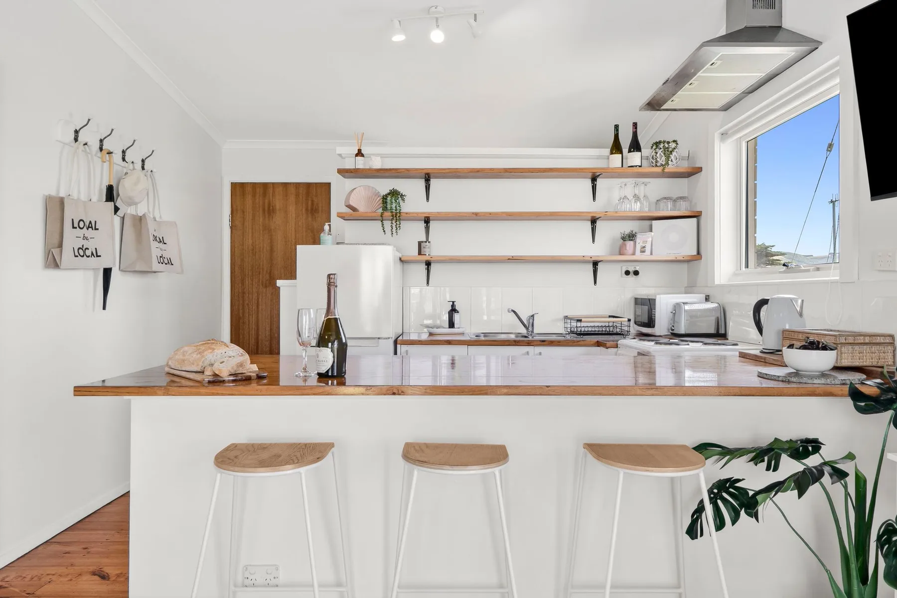 A bright kitchen with a long counter, open shelves, and stools.