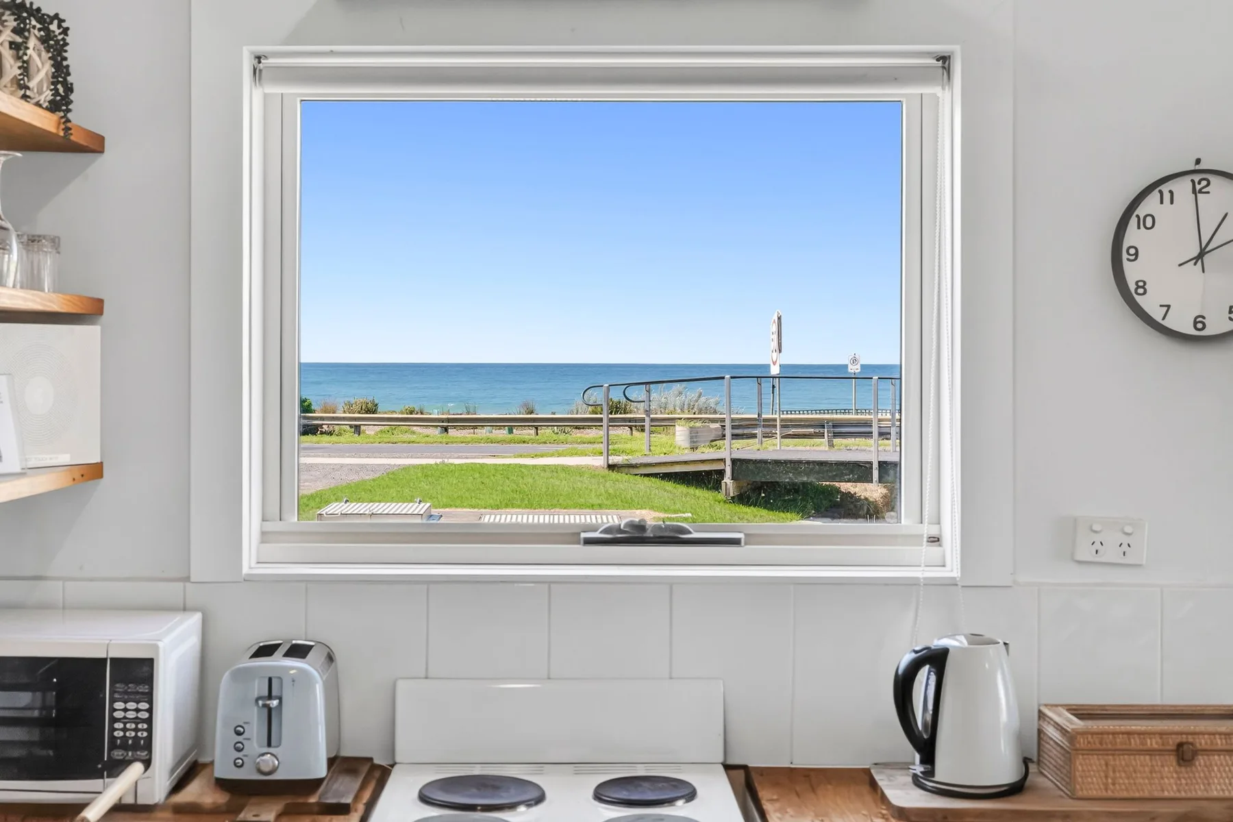 A kitchen window overlooks the ocean and a grassy area.