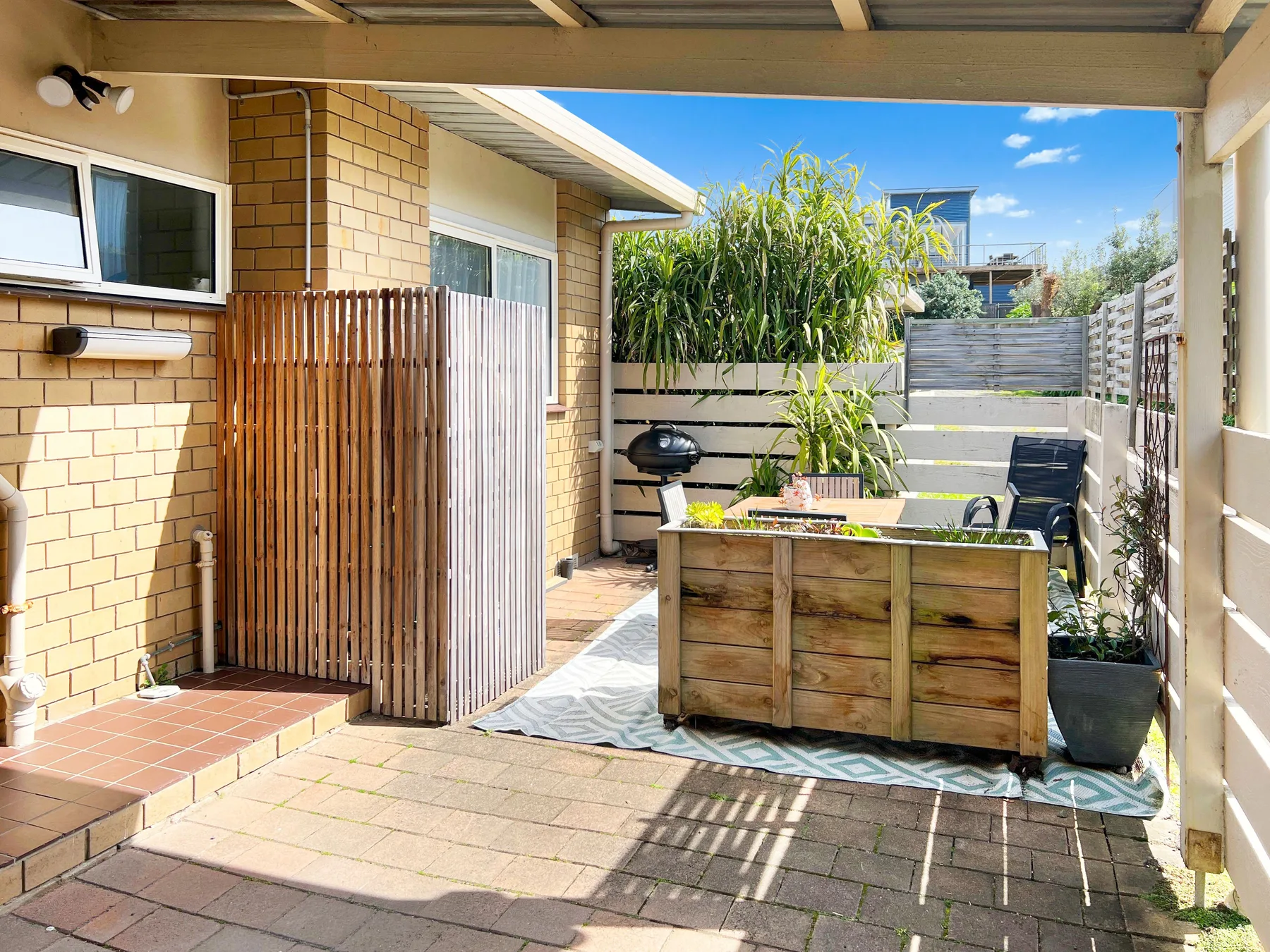A paved outdoor patio with a wooden planter and surrounding greenery.