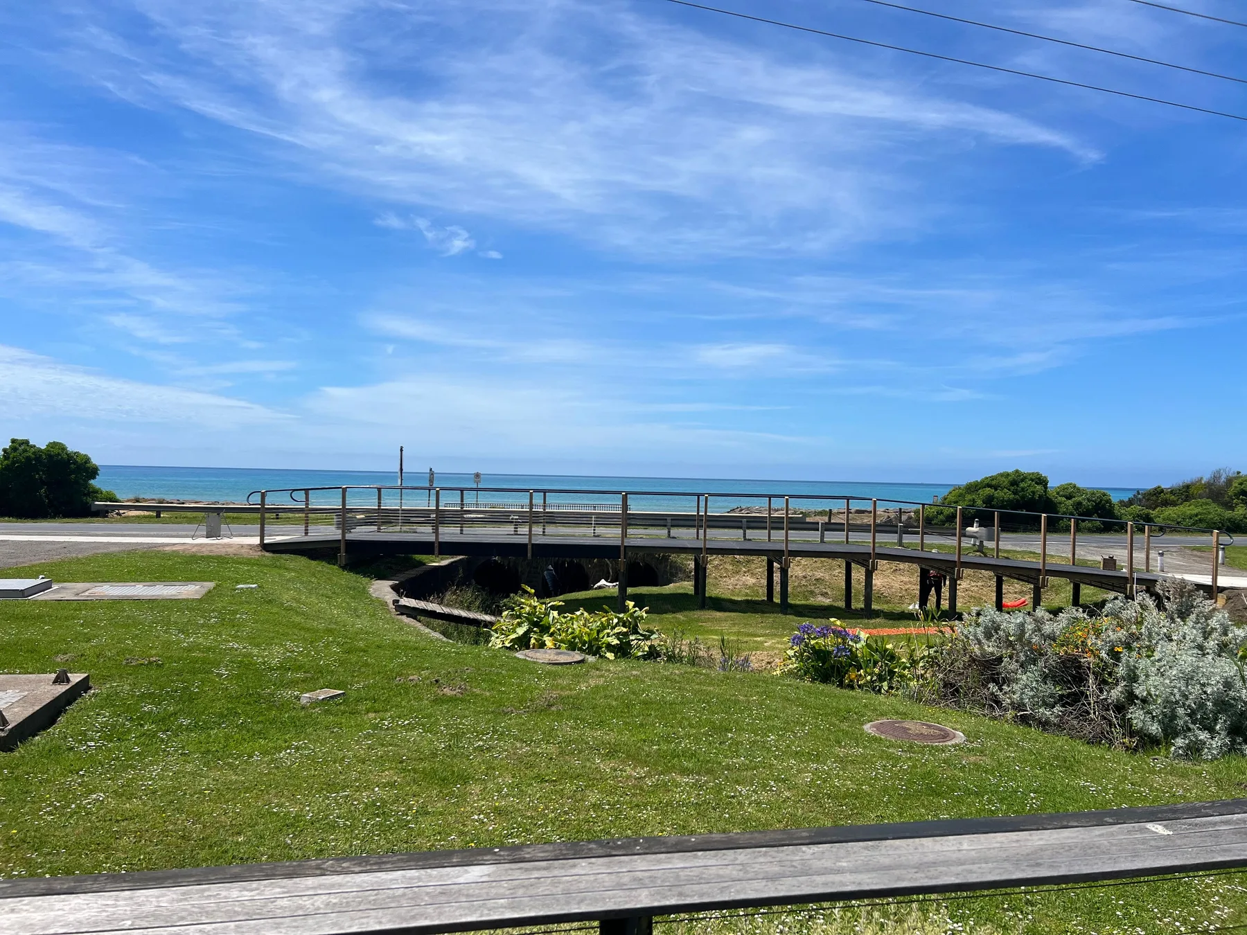 A grassy coastal landscape with a raised walkway and the ocean in the distance.