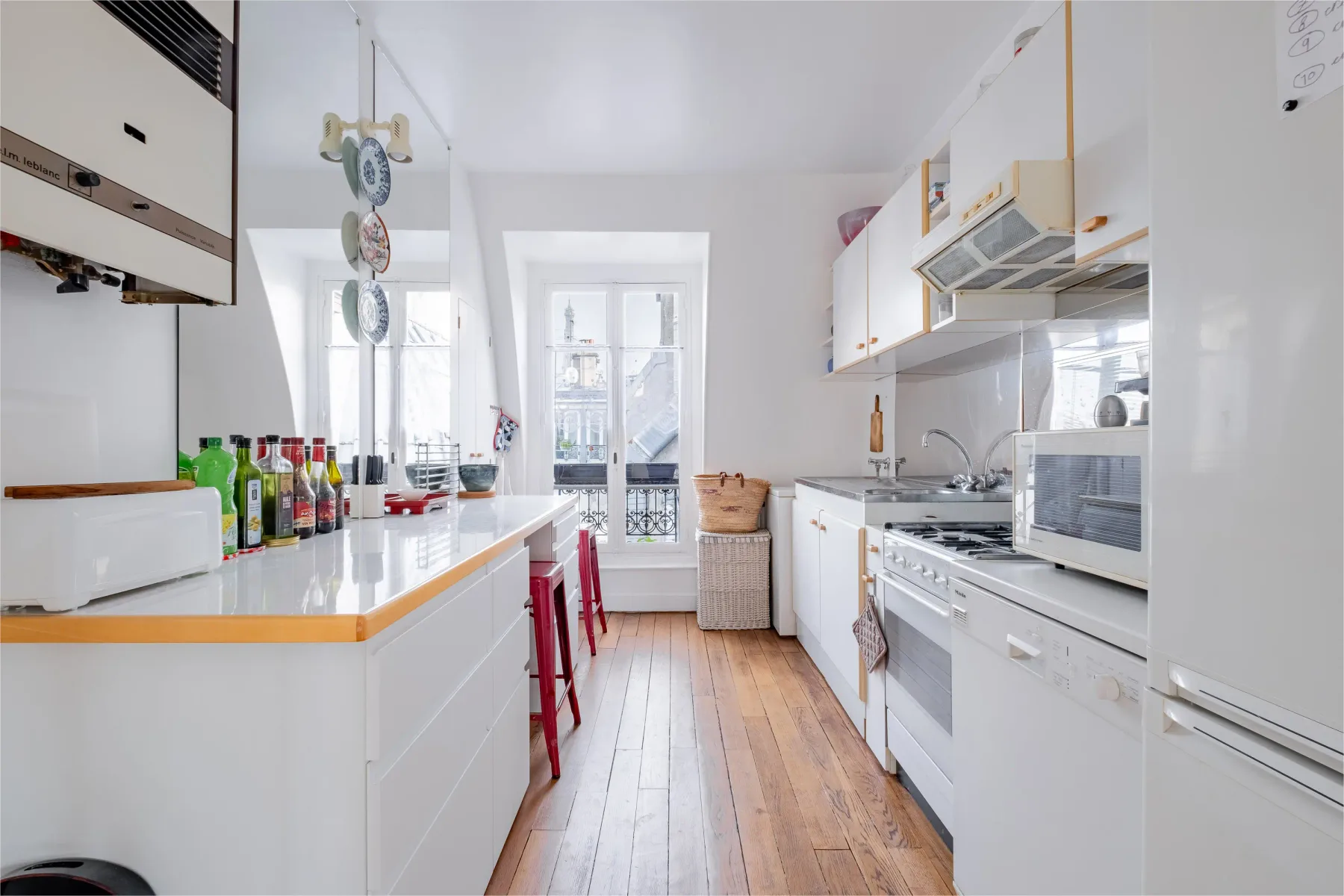 A bright narrow kitchen with white cabinets, counters, and a central walkway.