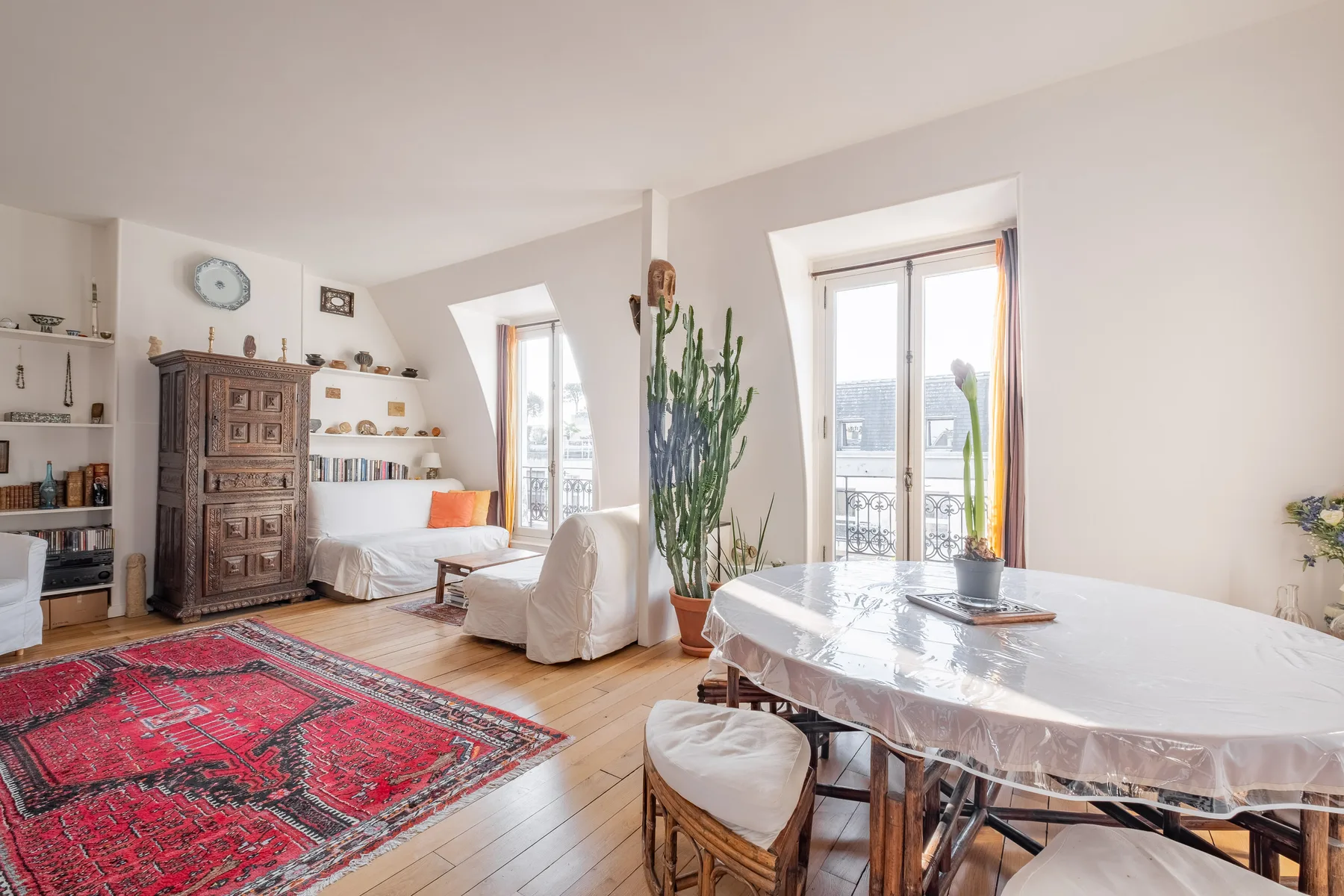 A bright living and dining room with a red patterned rug and a table by the windows.