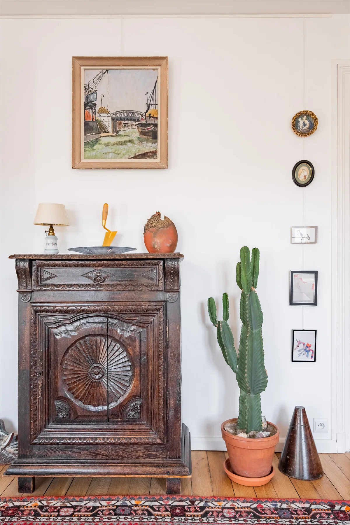 A carved wooden cabinet and potted cactus stand against a white wall.