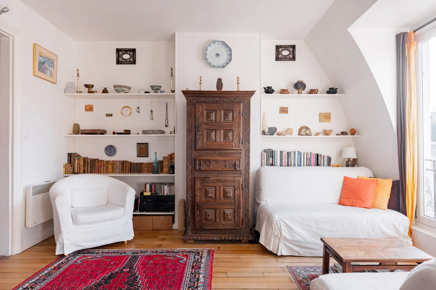 A bright living room with white seating, built-in shelves, and a patterned rug.