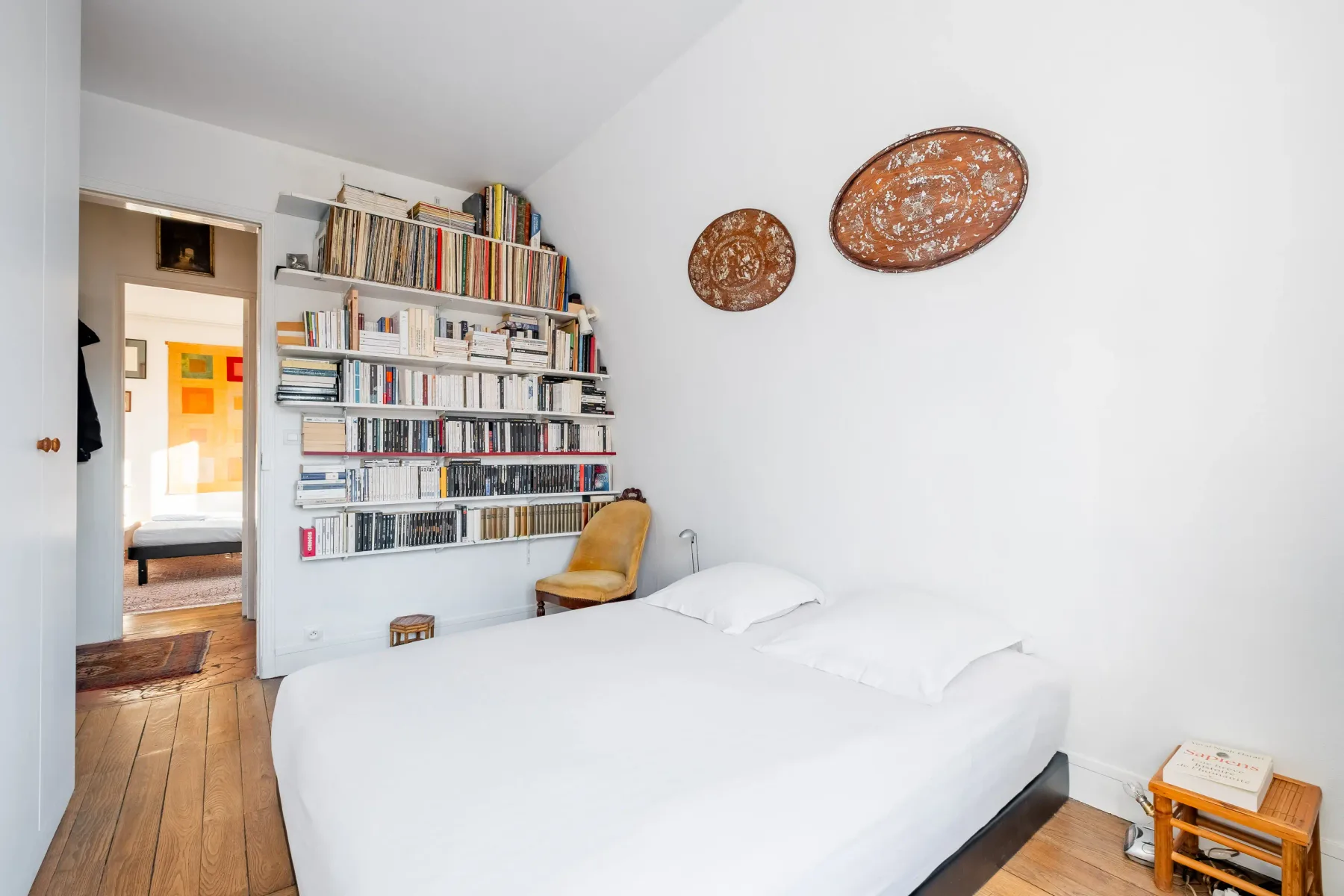 A bright bedroom with a bed and wall-mounted bookshelves.