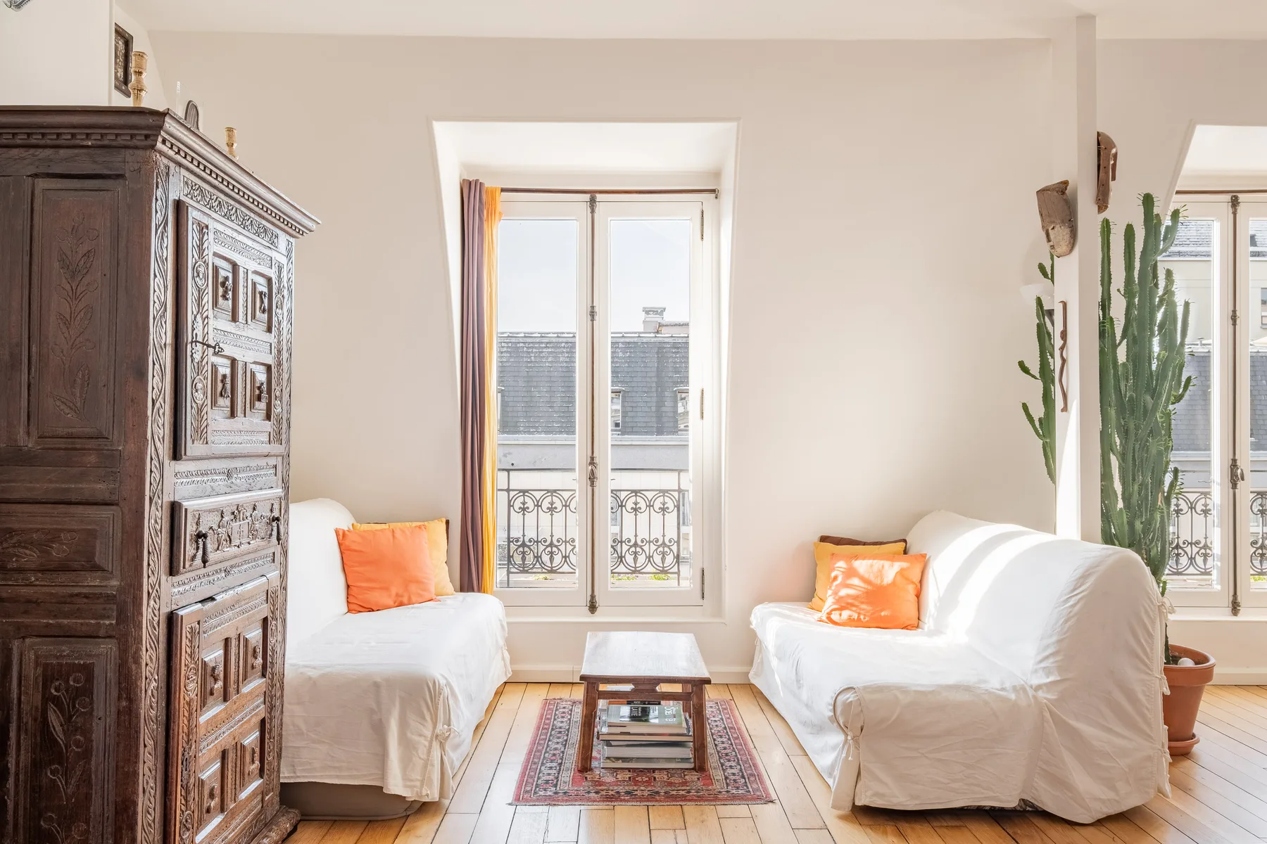 A bright living room with white seating, a low table, and tall windows.