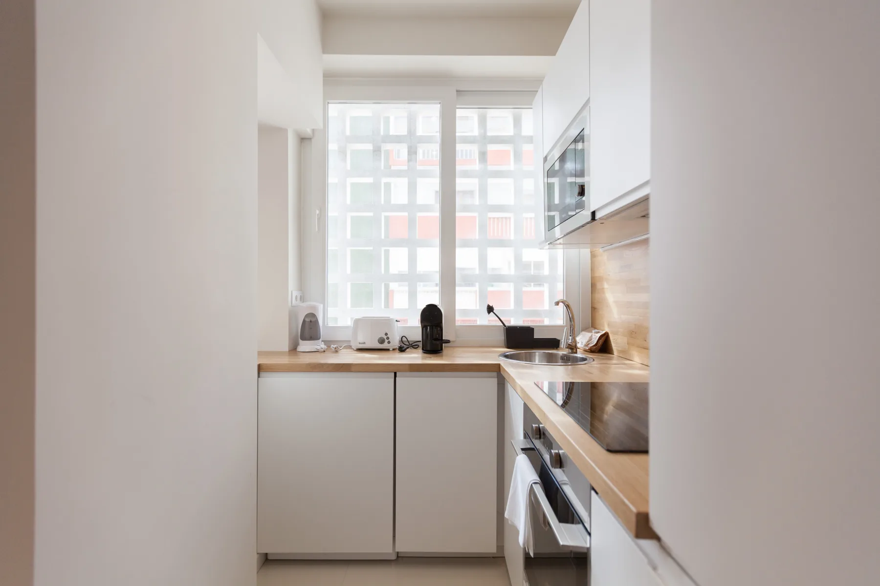 Una cocina estrecha con armarios blancos, encimera de madera y una ventana grande.