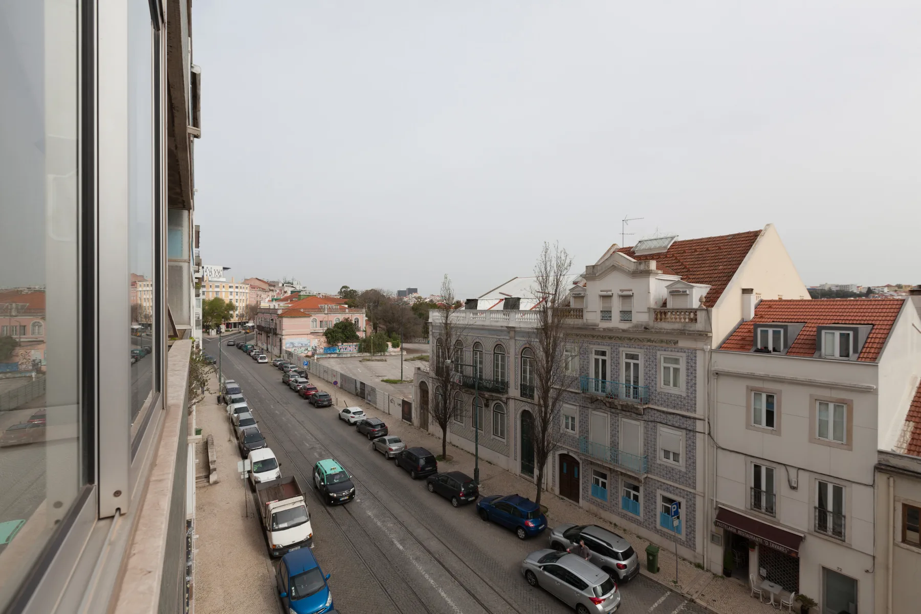 Una calle urbana con edificios y coches estacionados, vista desde una ventana.