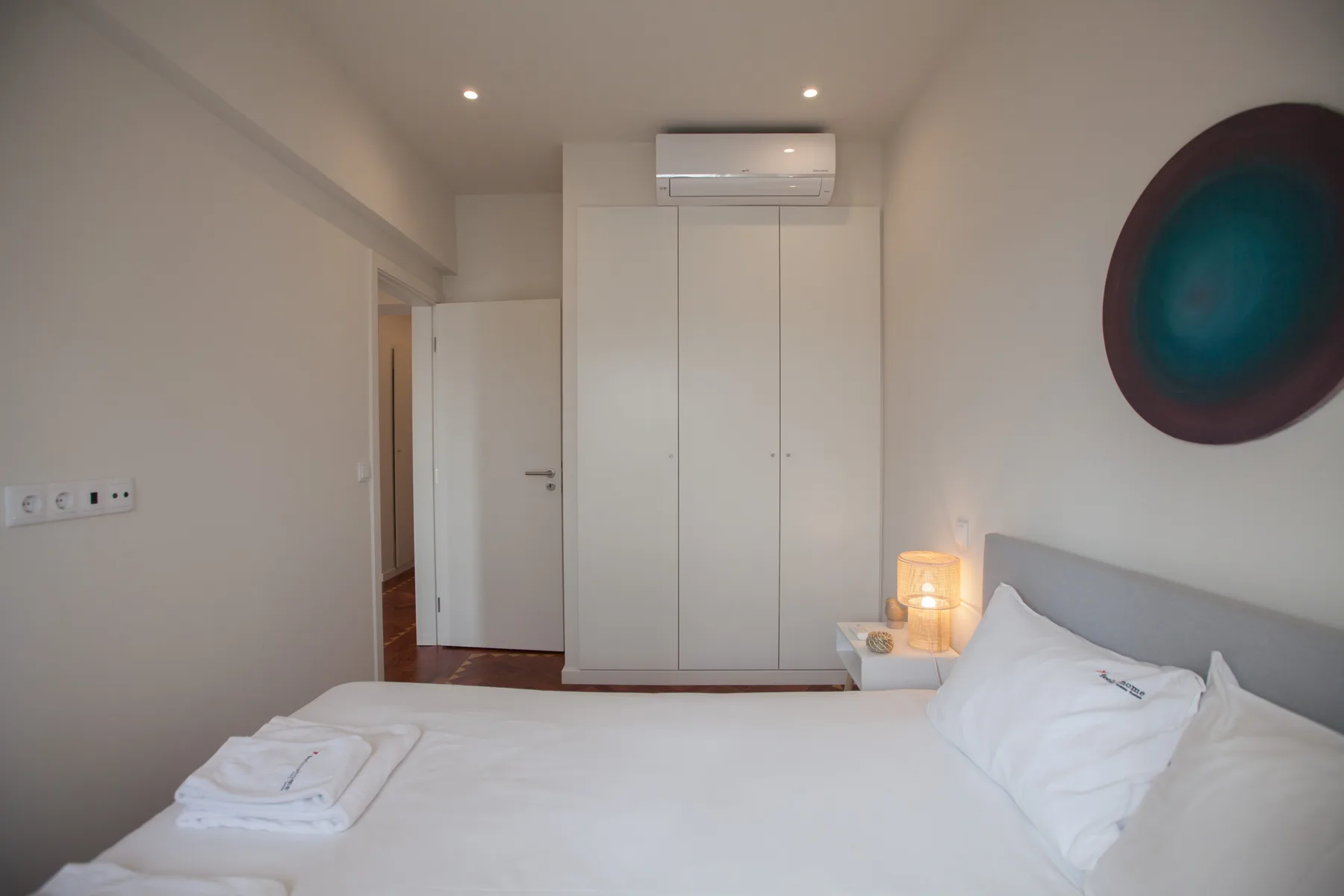 Un dormitorio con ropa de cama blanca, un armario y aire acondicionado en la pared.