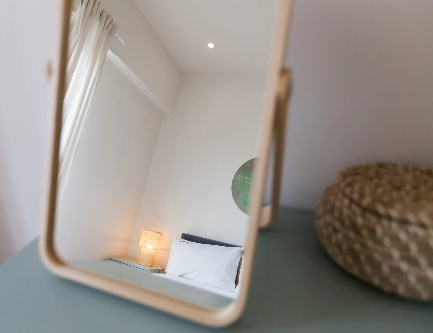 Un dormitorio reflejado en un espejo, con una cama y una lámpara de mesilla.