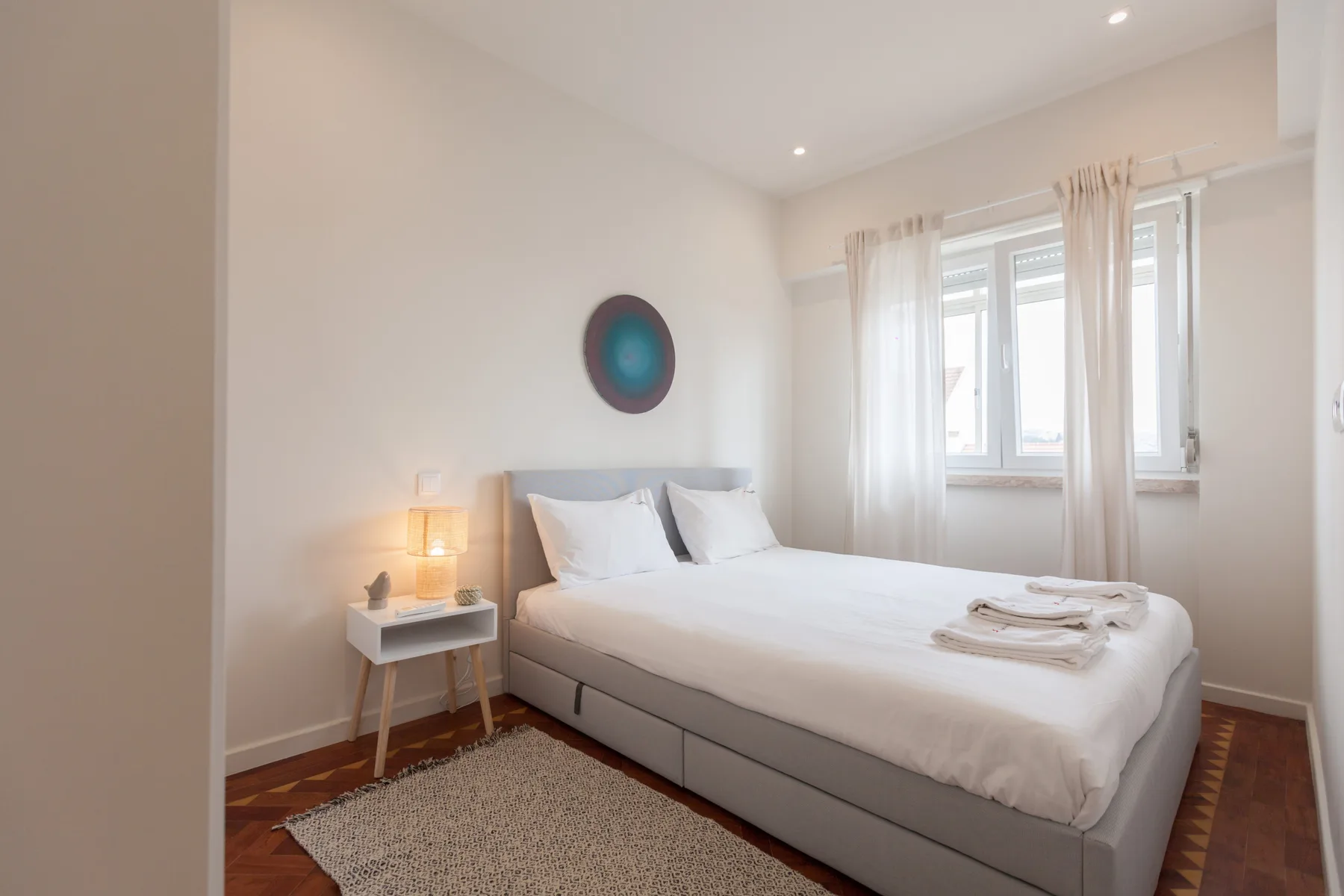 Un dormitorio luminoso con una cama y una ventana con cortinas claras.