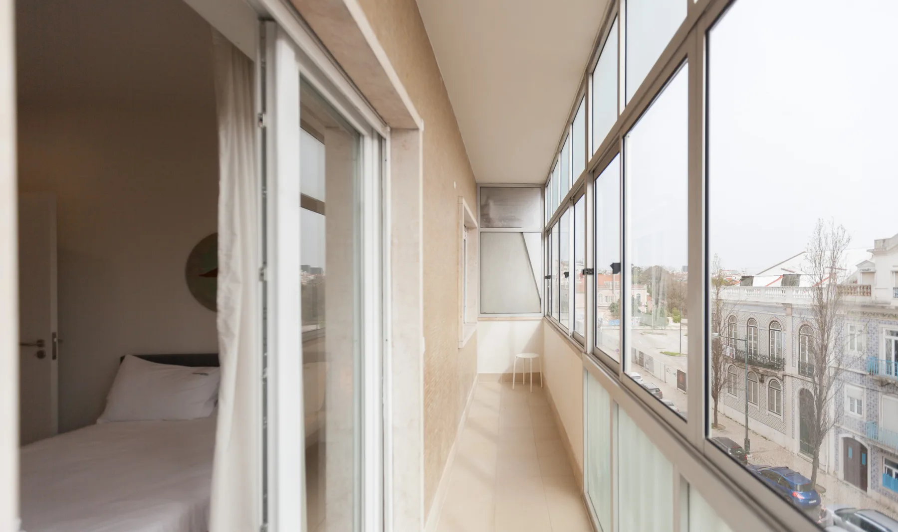 Un pasillo acristalado junto a un balcón recorre el exterior de un dormitorio con cama.