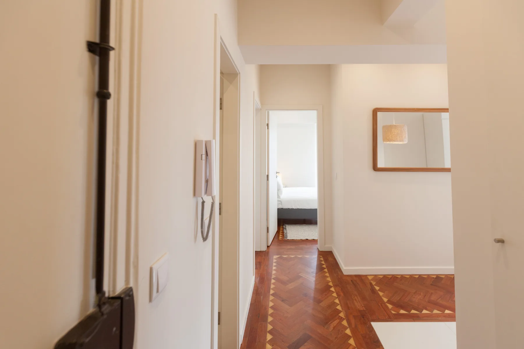 Un pasillo luminoso con suelo de madera conduce a una habitación con una cama.