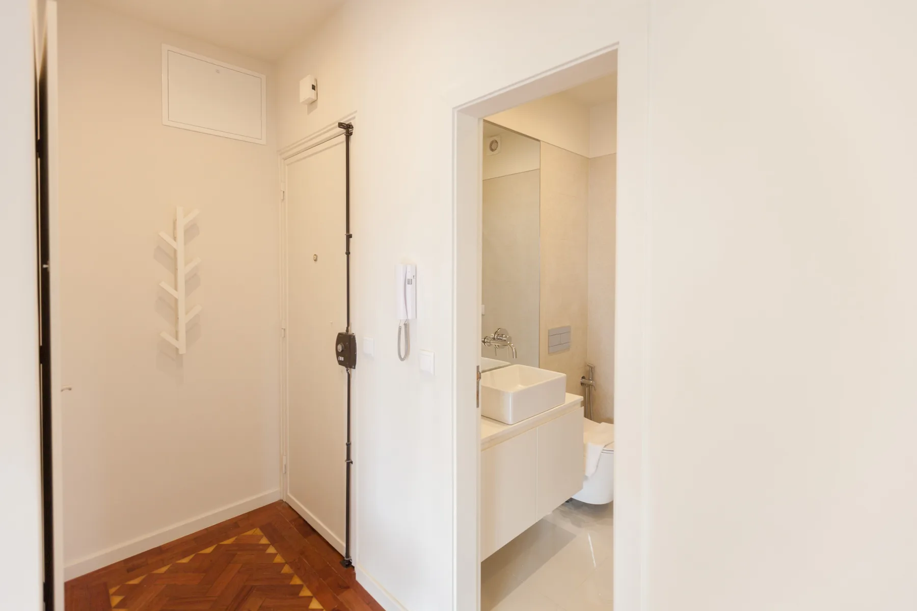 Un pasillo luminoso da a un baño con lavabo e inodoro.