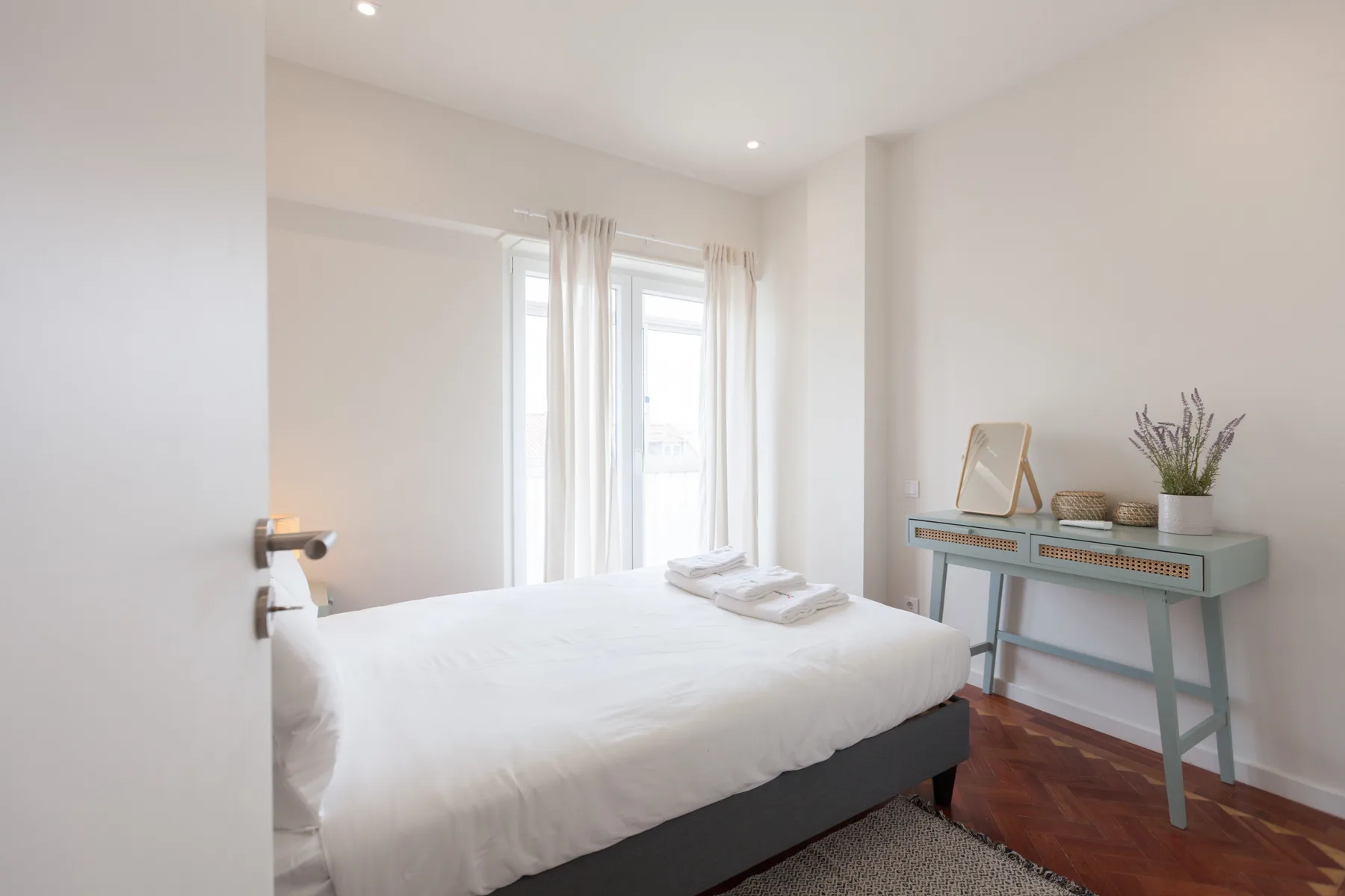 Un dormitorio luminoso con una cama bien hecha y un escritorio junto a la ventana.