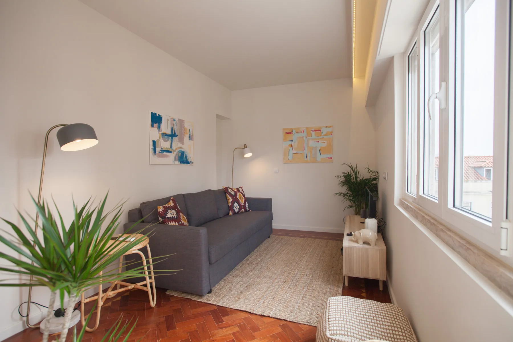 Una sala luminosa con un sofá, una alfombra y grandes ventanas.