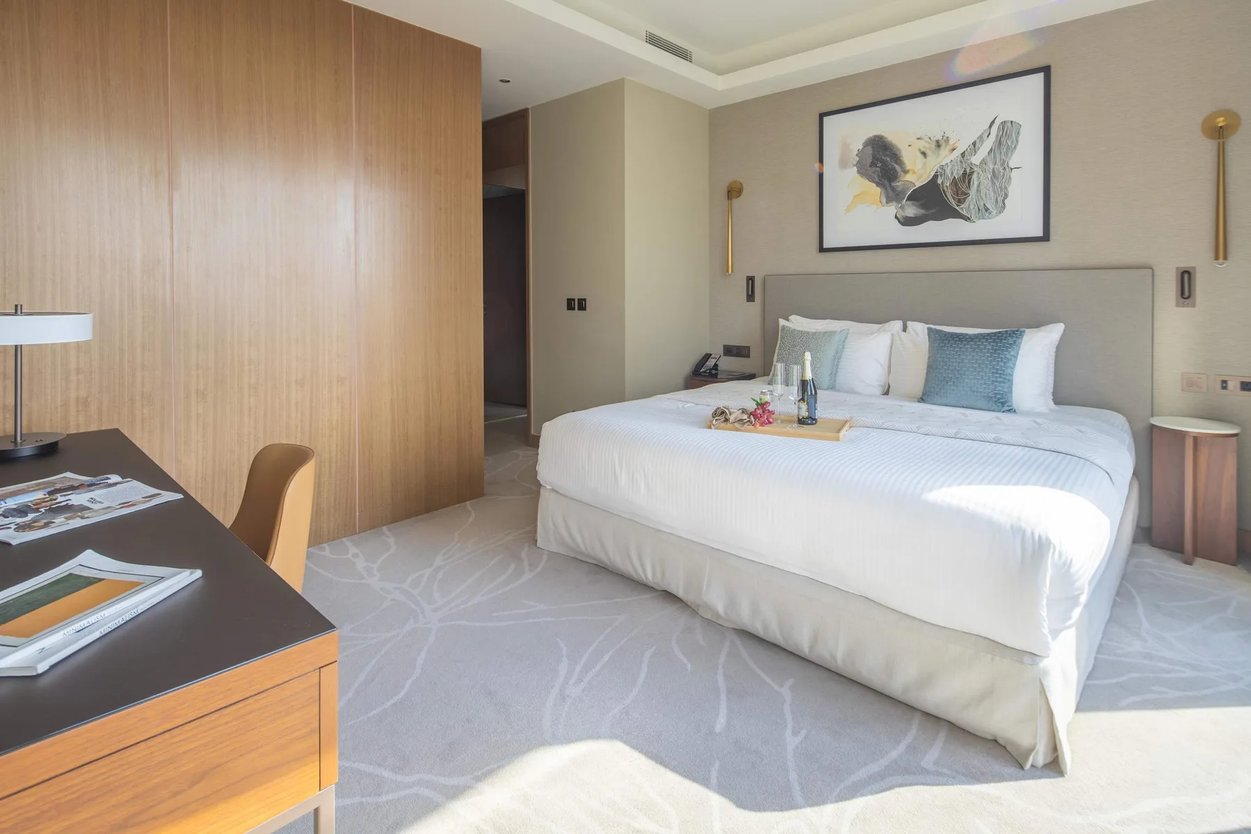 A bedroom with a neatly made bed, framed artwork, and a desk.