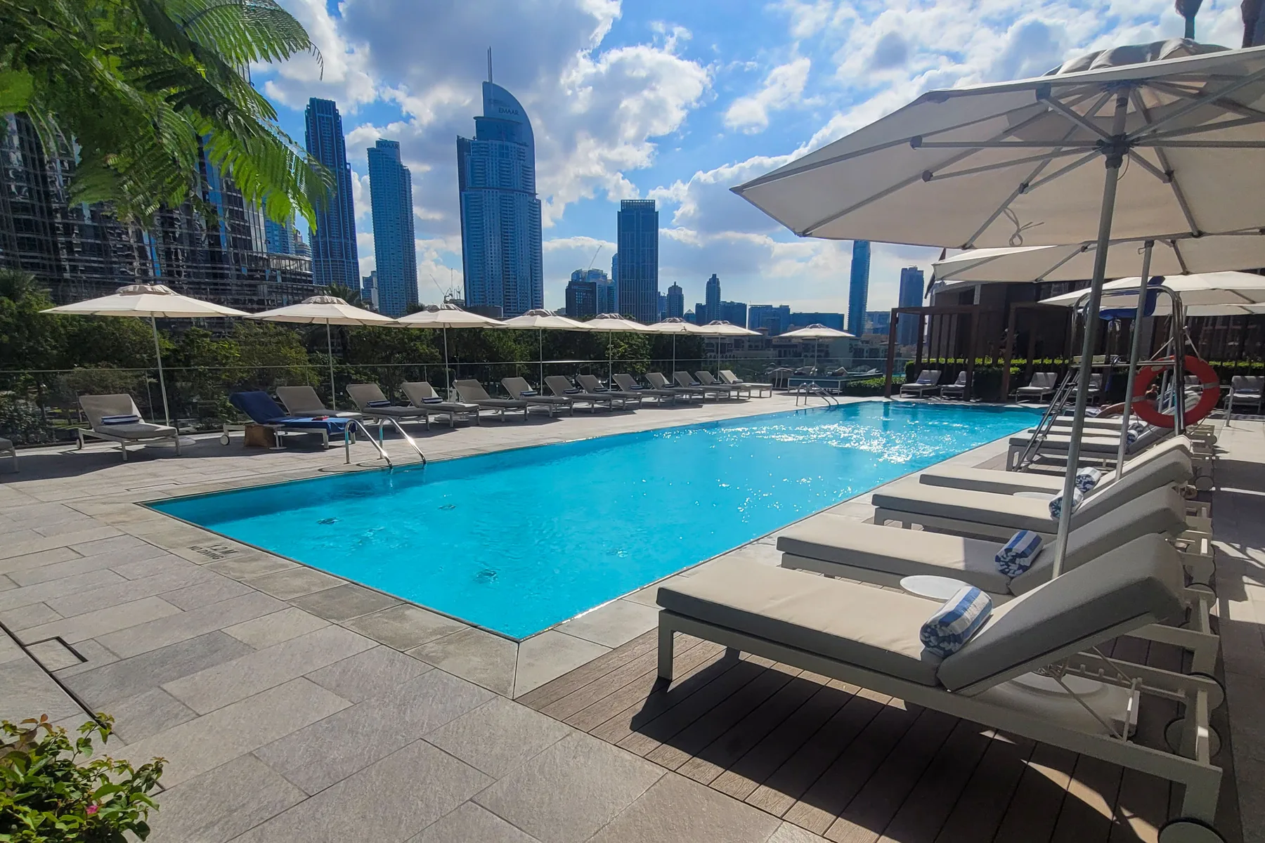 An outdoor swimming pool is surrounded by lounge seating and umbrellas.