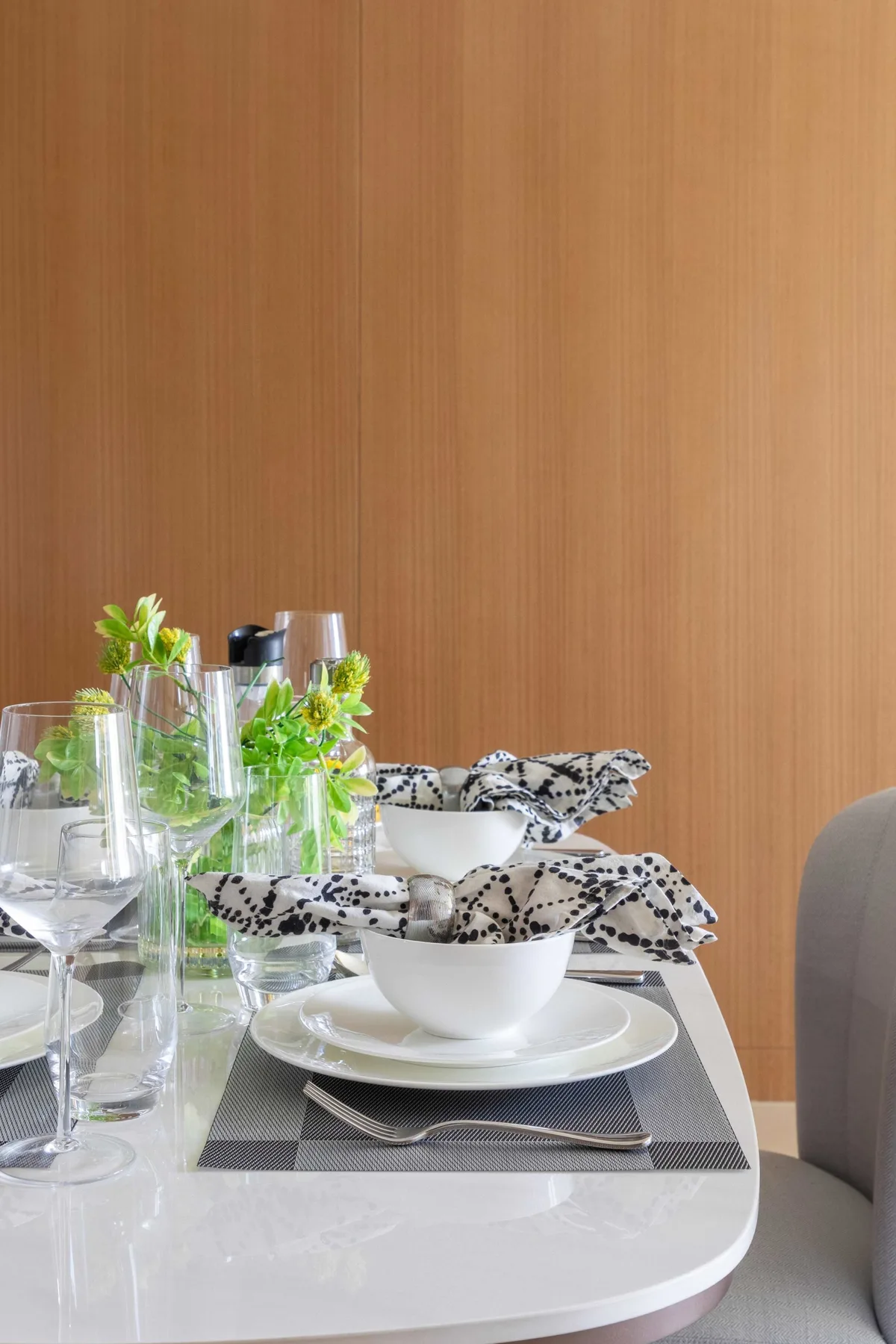 A dining table is set with white dishes, glassware, and greenery.