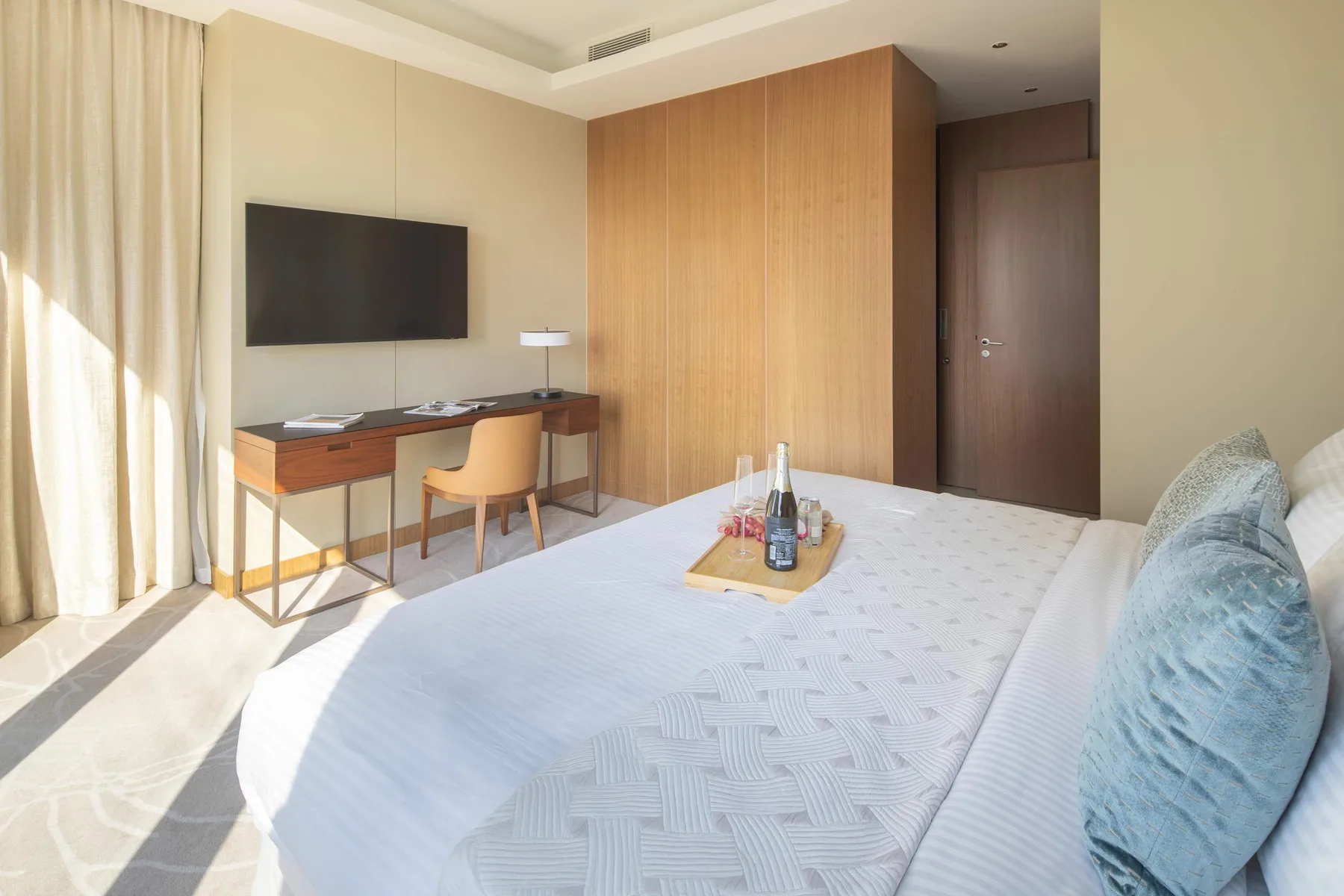 A bright bedroom with a bed, desk, and wall-mounted television.