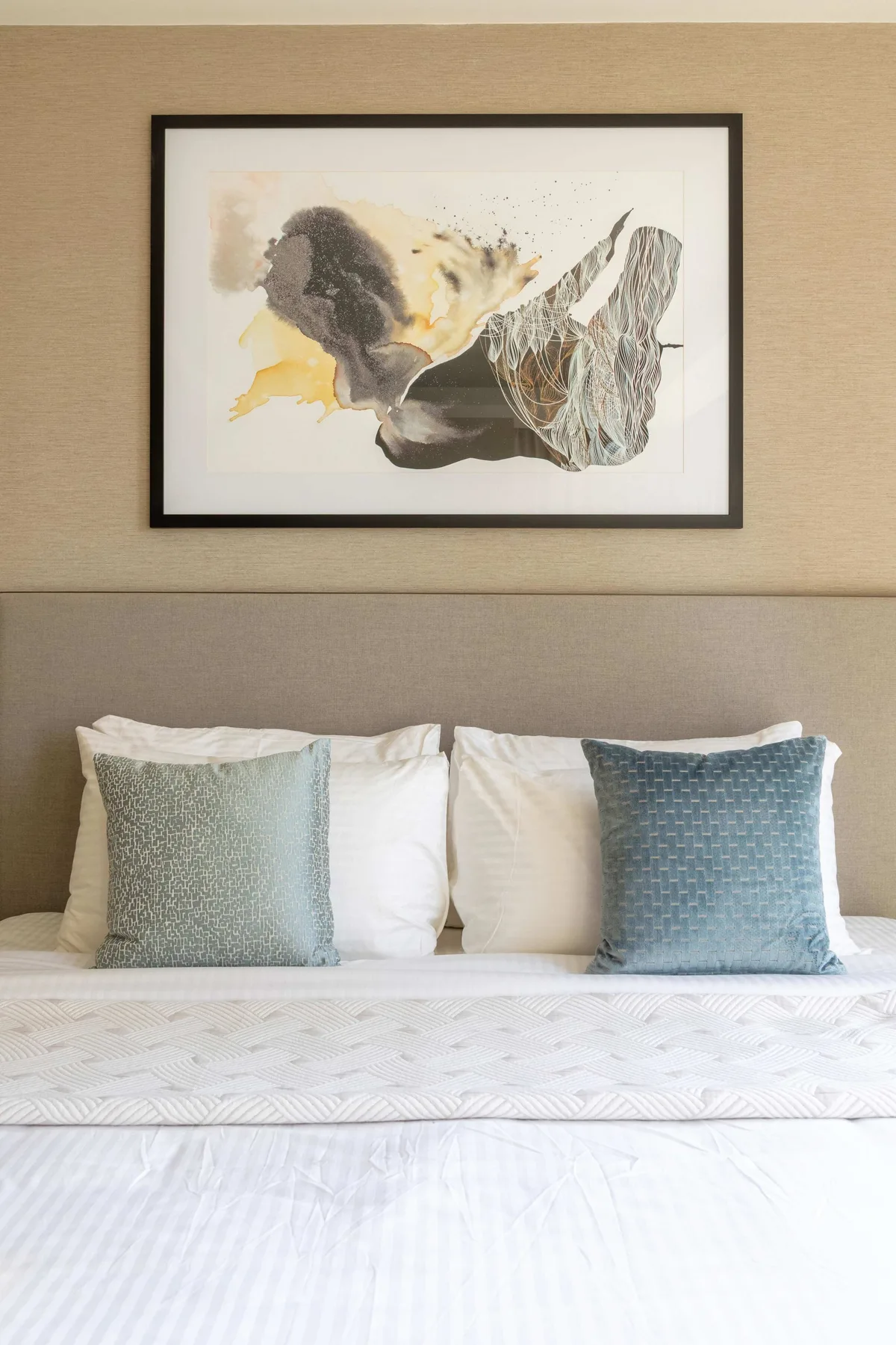 A neatly made bed with white bedding and two pillows sits beneath framed abstract artwork.