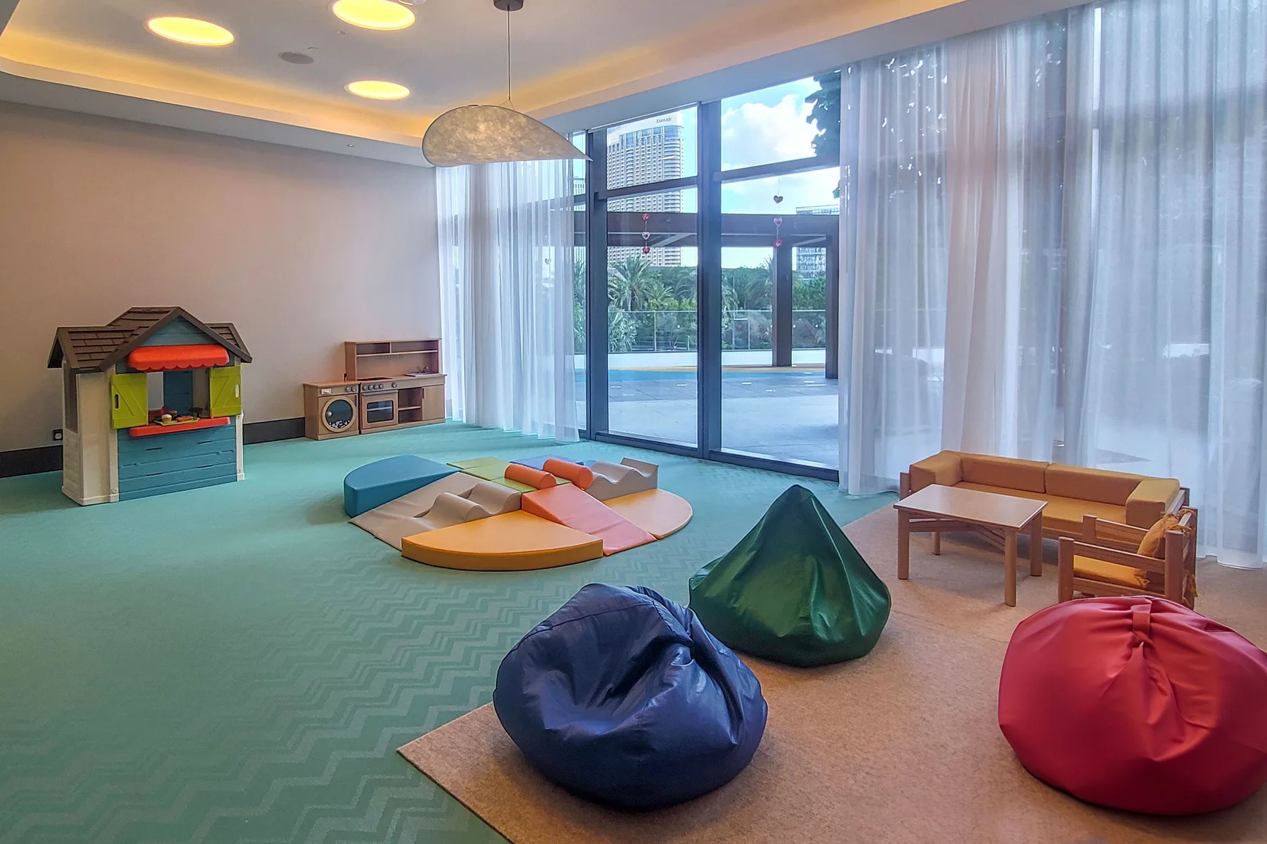 A bright playroom with floor cushions, a playhouse, and large windows.